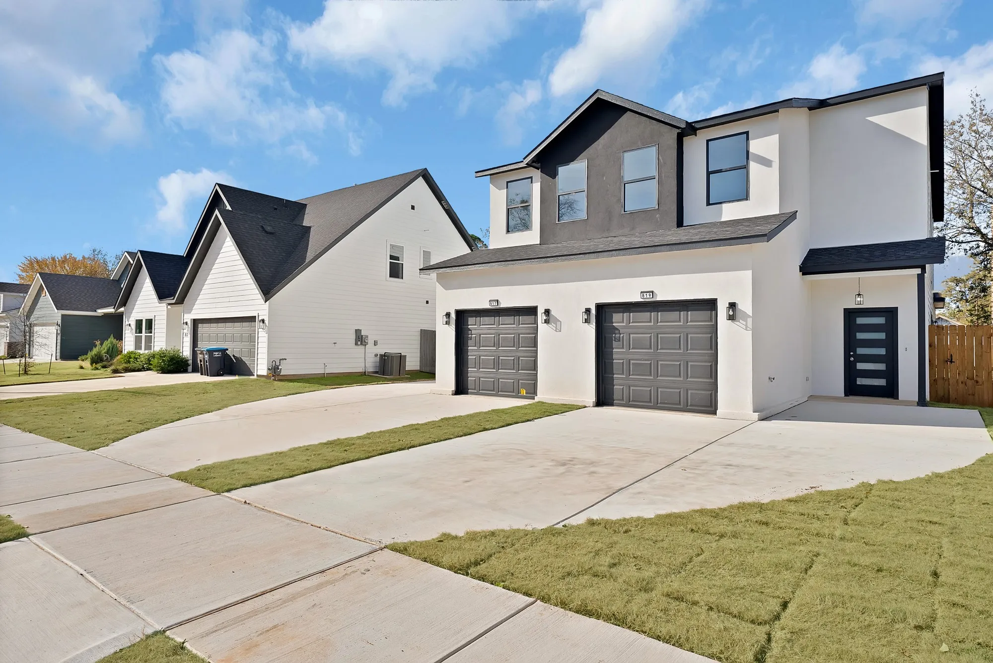 Modern architecture featuring a two-car garage, white stucco exterior with dark trim accents, and a contemporary front door