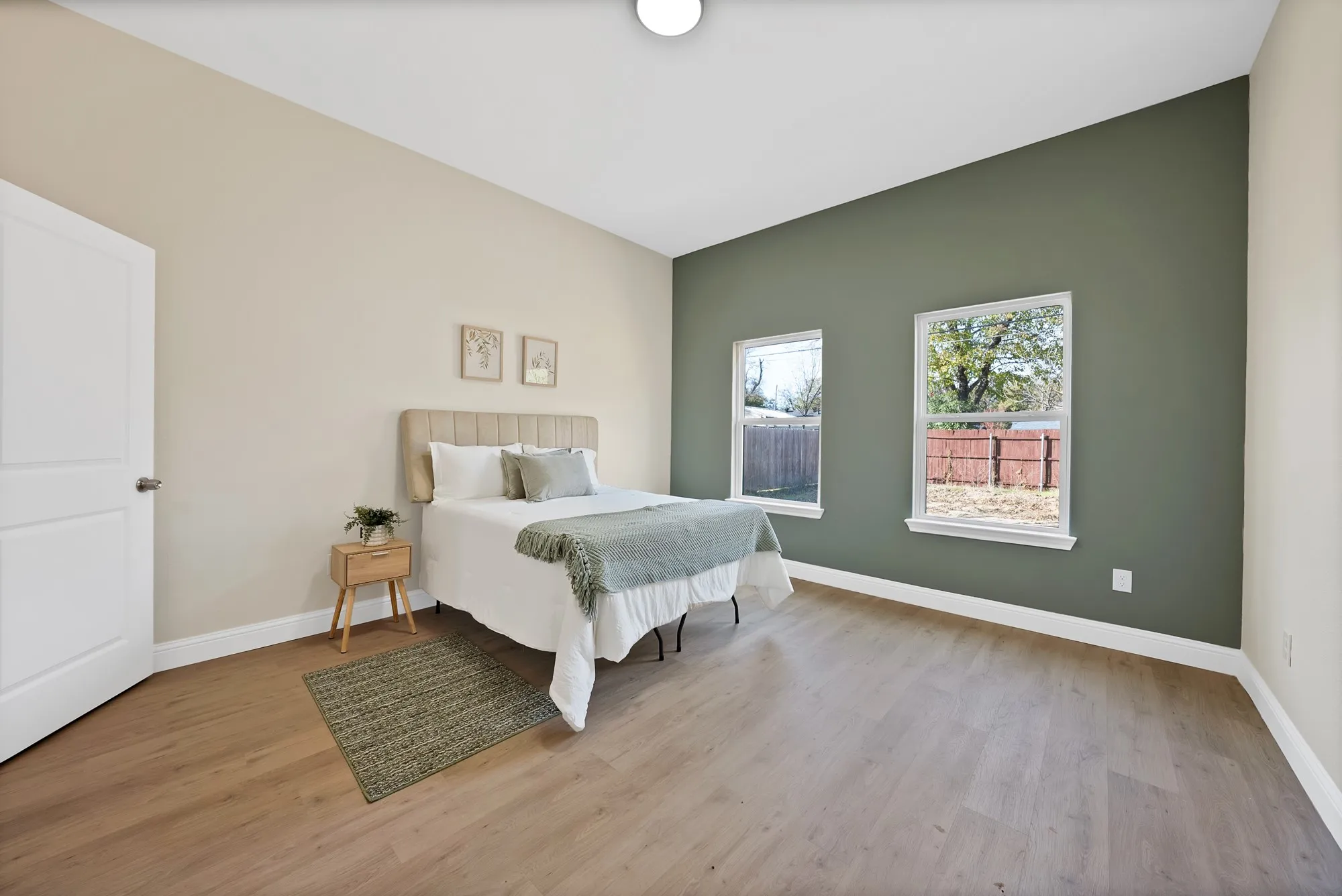Spacious room featuring wood-finish flooring, a contemporary accent wall, two large windows, and a white paneled door