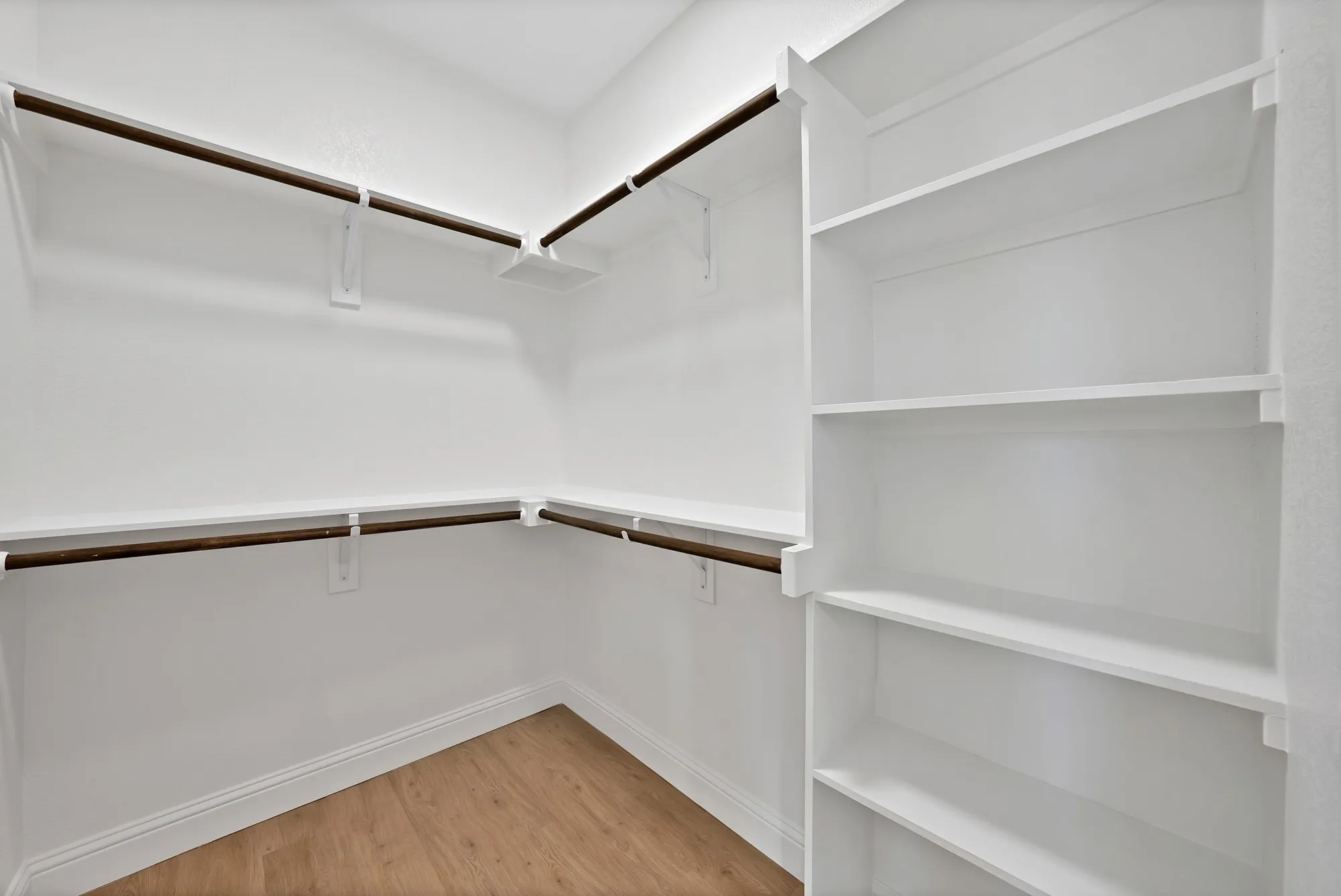 Walk-in closet featuring light wood-finish flooring, white walls, built-in shelving, and multiple clothing rods