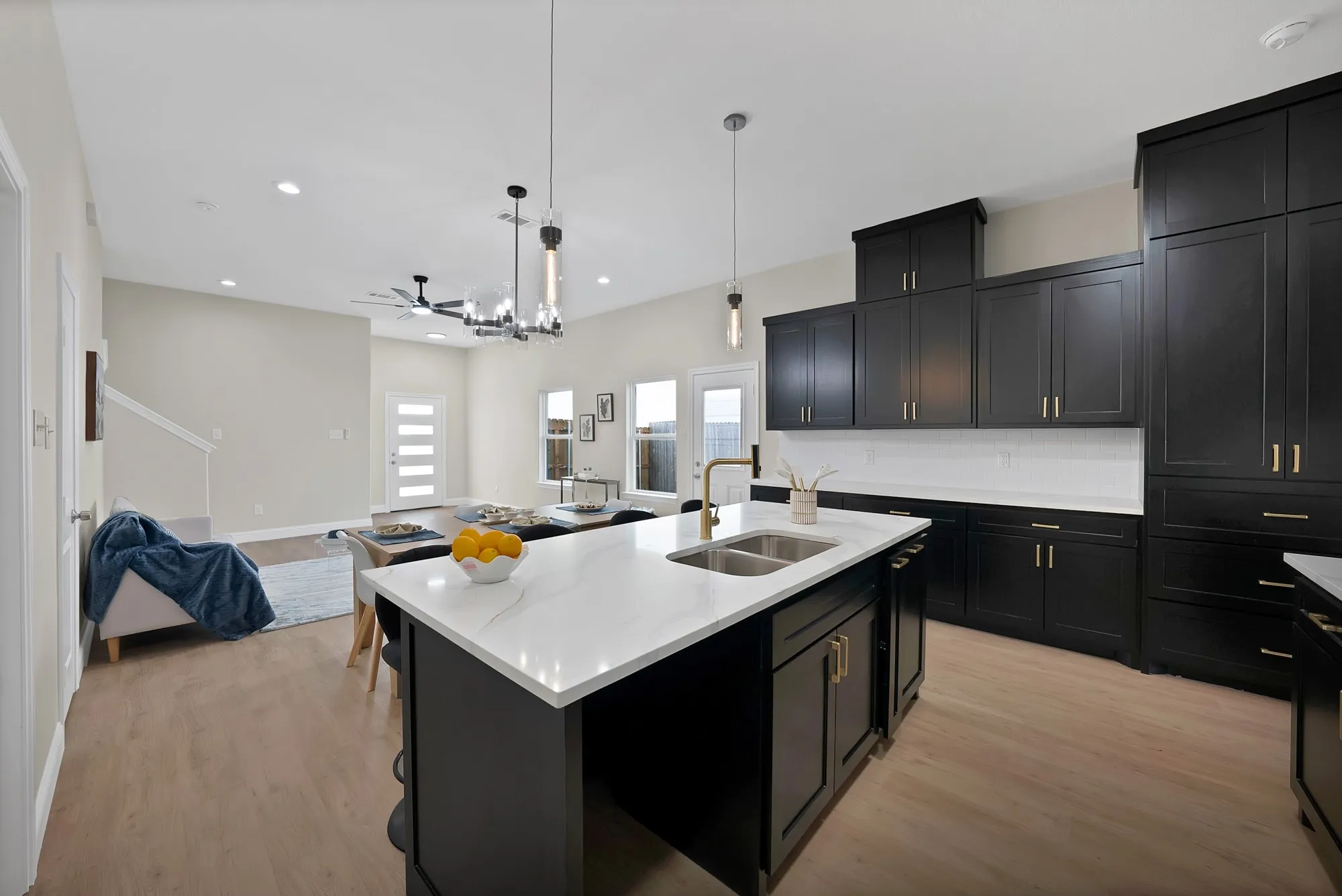 Modern kitchen featuring dark cabinetry with gold-tone hardware, white countertops, and a full-height white subway tile backsplash