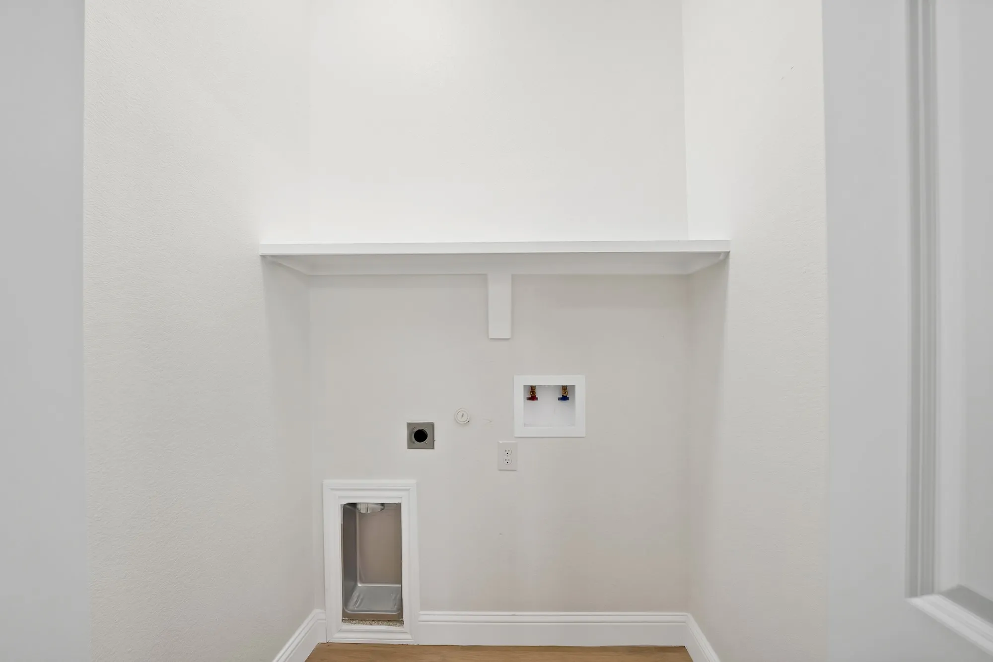 Dedicated laundry area with a utility sink hookup, water connections, and a single wall shelf