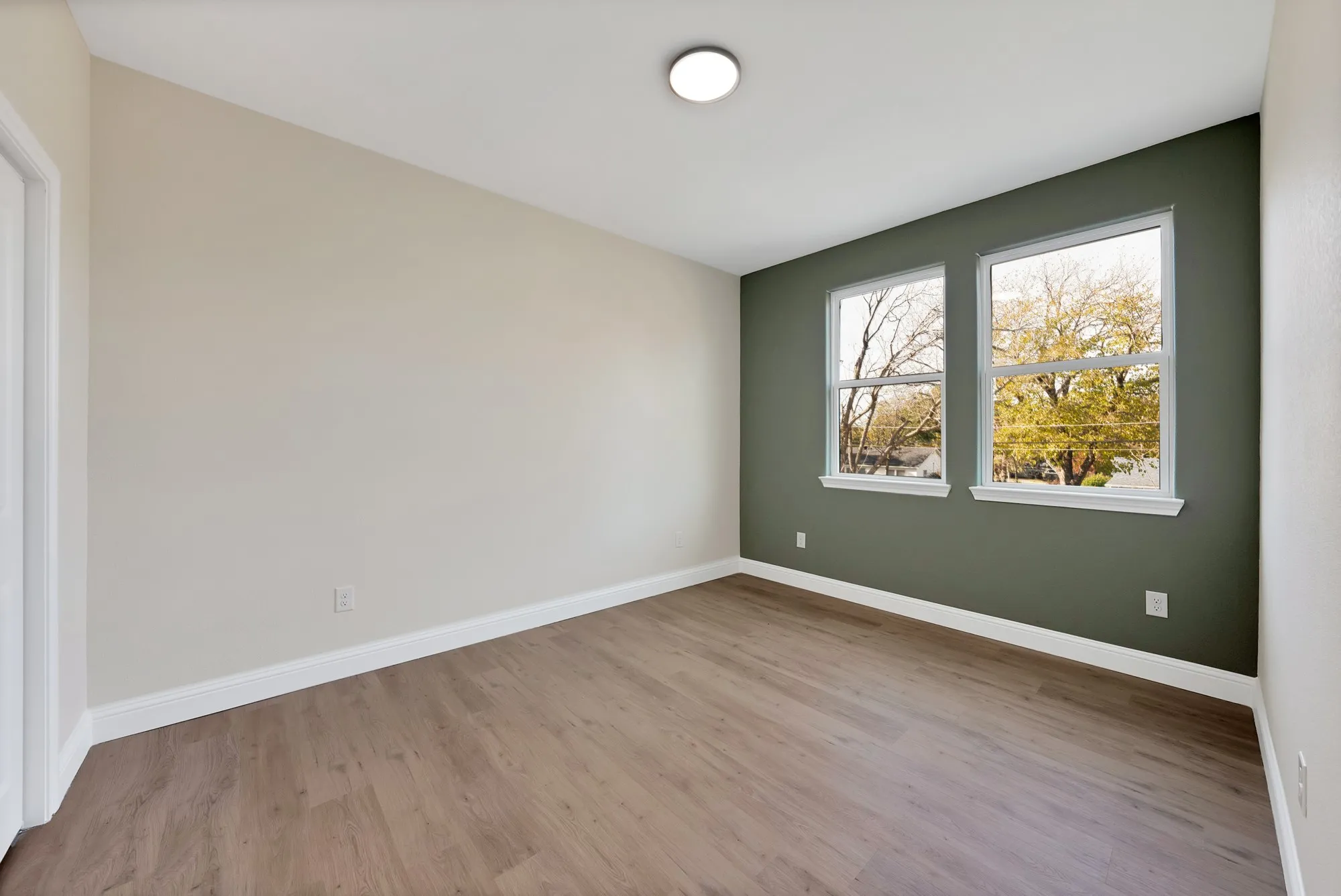 Room featuring wood-finish flooring, white baseboards, and two windows