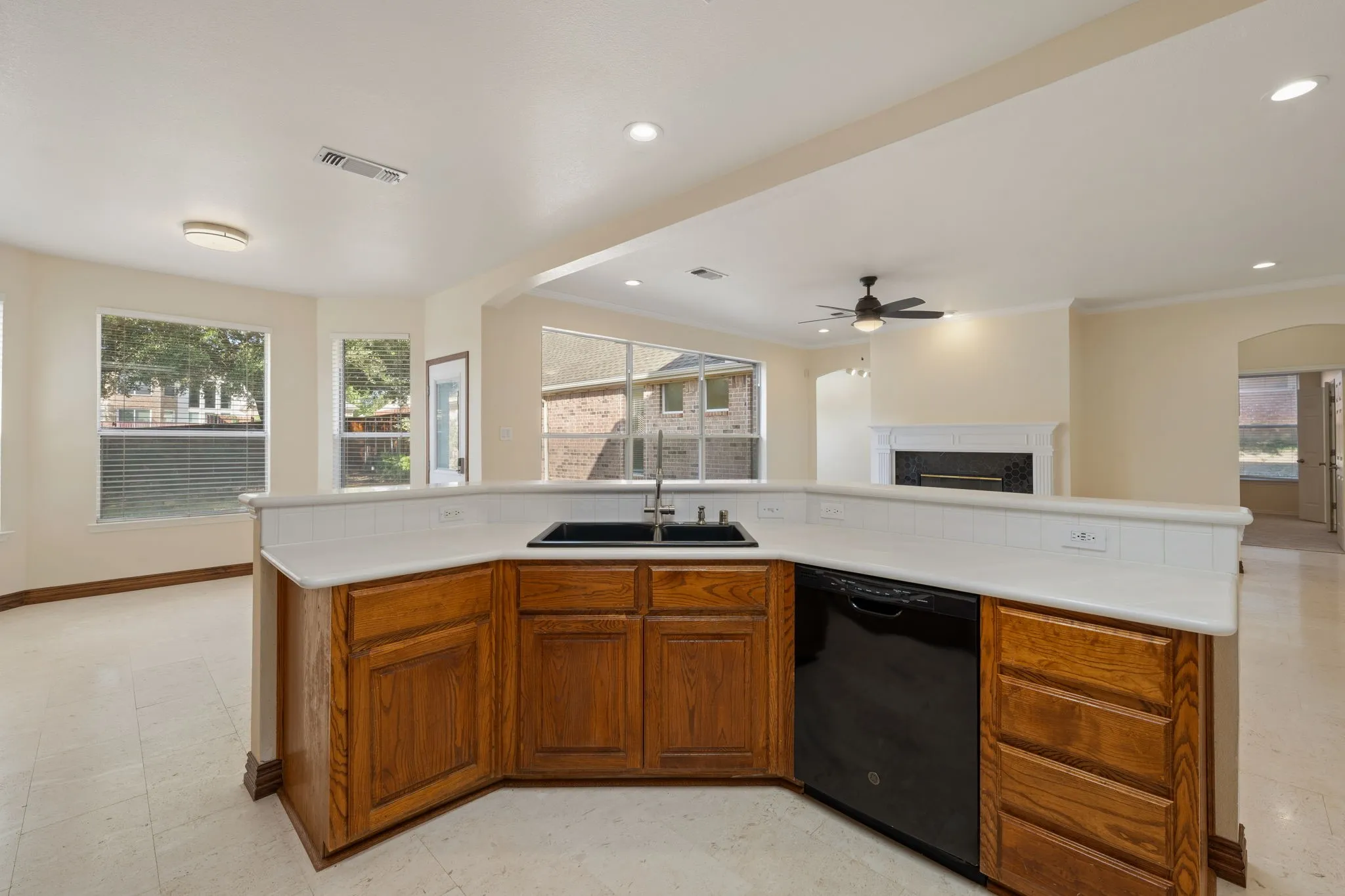 Kitchen island with a black sink and built-in dishwasher, featuring wood cabinetry and light-toned countertops