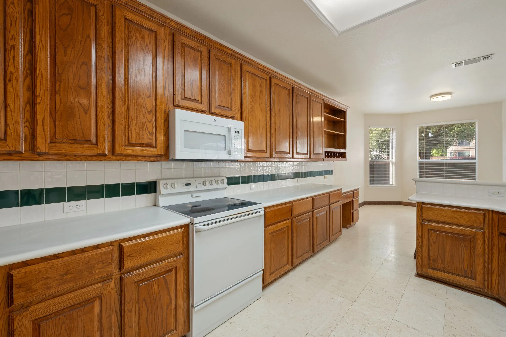 Kitchen featuring extensive wood cabinetry, white countertops, tile flooring, a built-in microwave, and a tile backsplash with a decorative accent band