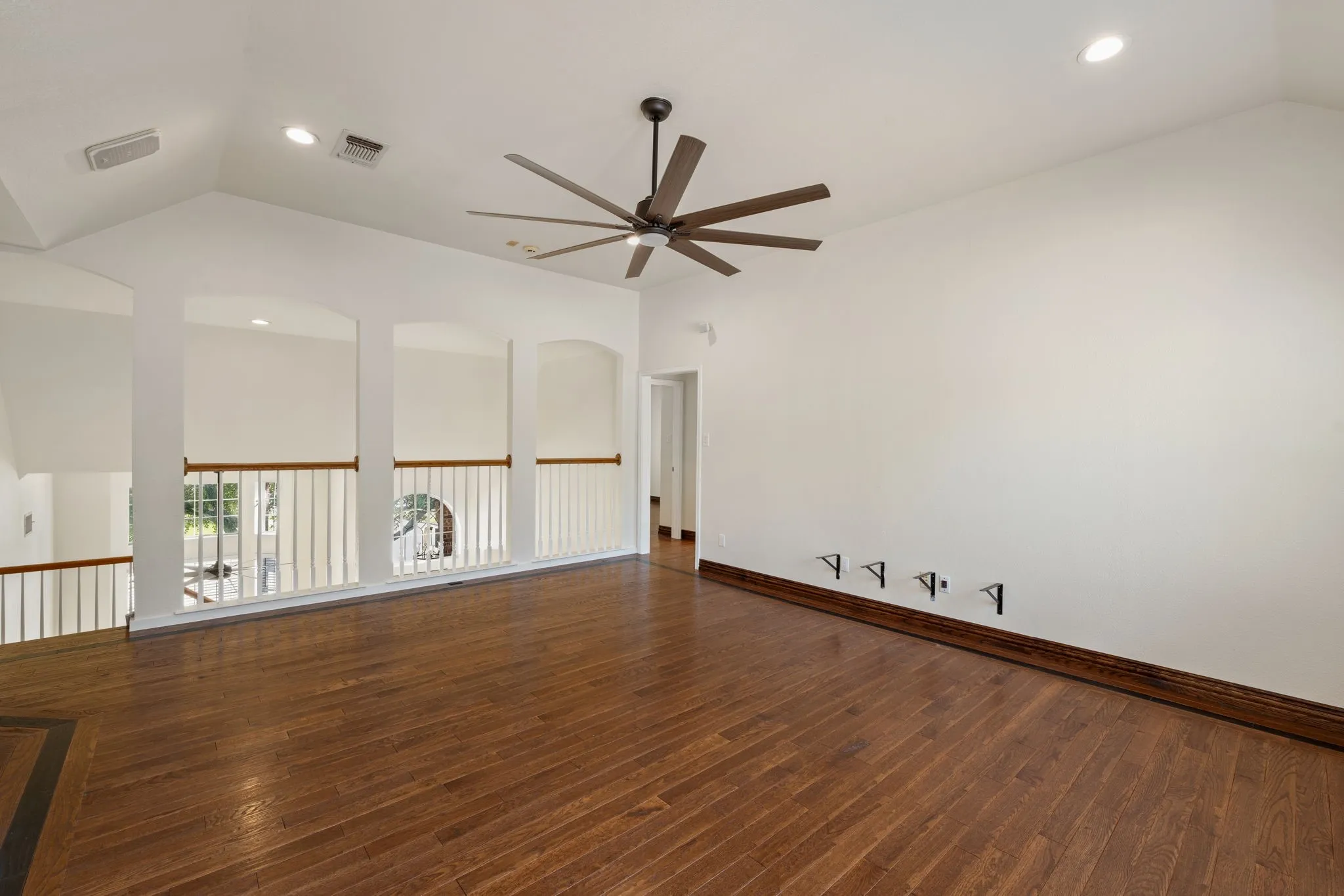 Upstairs loft space with vaulted ceilings, recessed lighting, a contemporary ceiling fan, wood-finish flooring, and a decorative architectural railing overlooking the floor below
