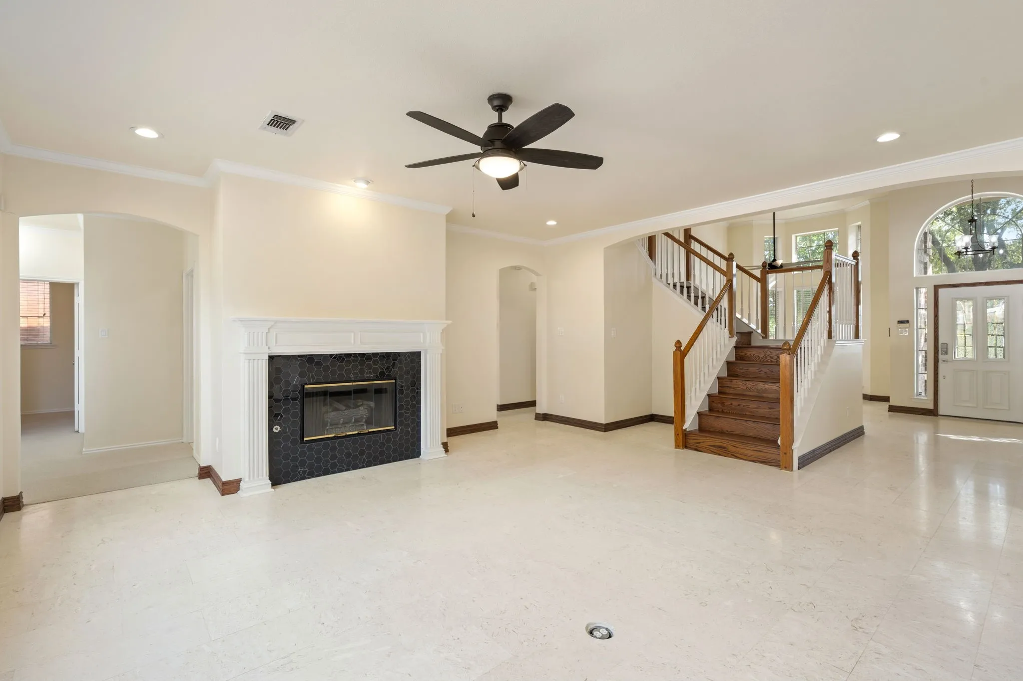 Open concept living area featuring light-toned tile flooring, a fireplace with a dark tile surround and white mantel, and a dark-toned ceiling fan