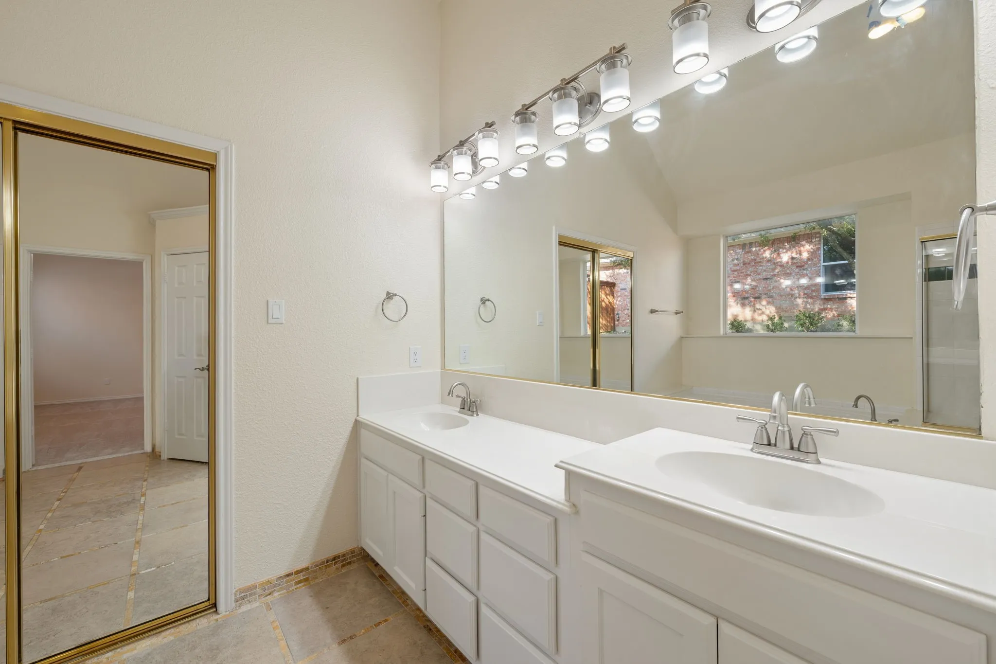 Dual vanity with white cabinetry and integrated sinks, large wall-mounted mirror, and multi-bulb overhead lighting fixture