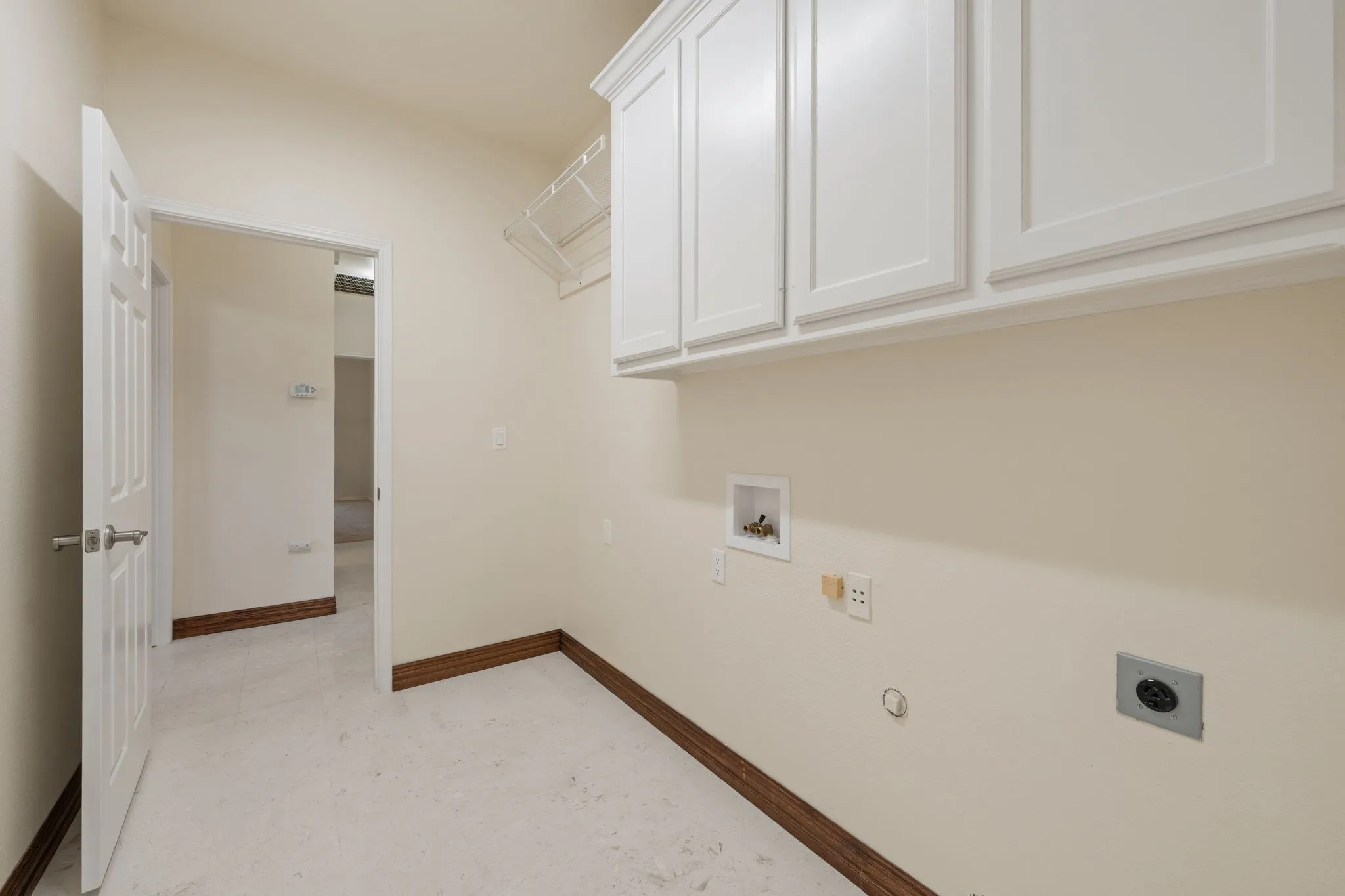 Laundry area featuring white shaker-style cabinetry, a wire storage shelf, and light-toned walls with dark wood-finish trim