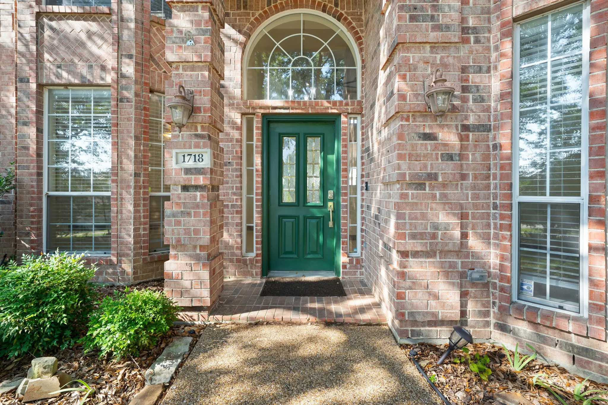 Brick facade with a vibrant green entry door, transom window, and sidelights