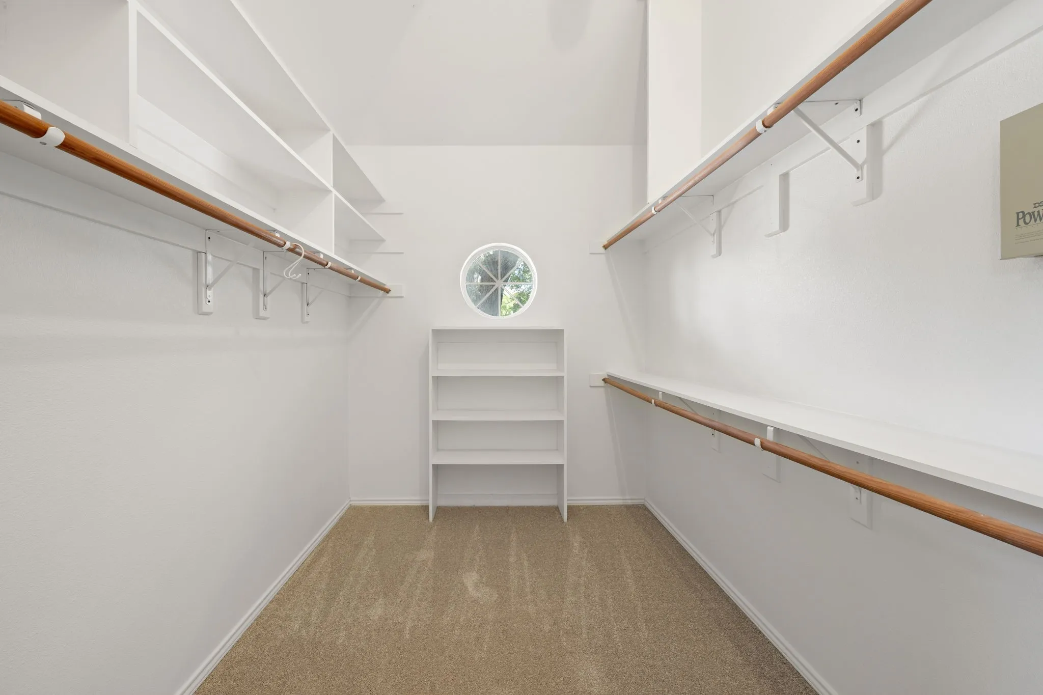 Walk-in closet featuring white walls, carpet flooring, a circular window, built-in shelving, and dual clothes hanging rods