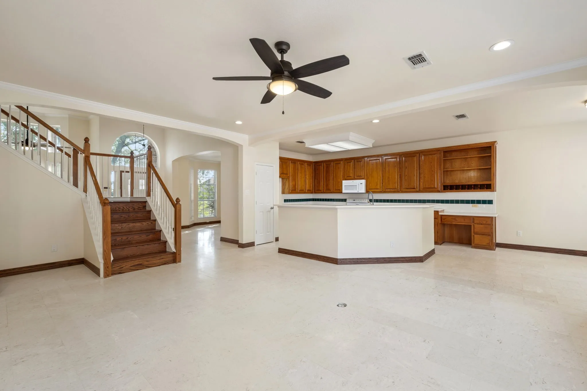 Open-concept living area featuring light-toned flooring, a staircase with wood-finish treads and white risers, and a kitchen island with built-in cabinetry