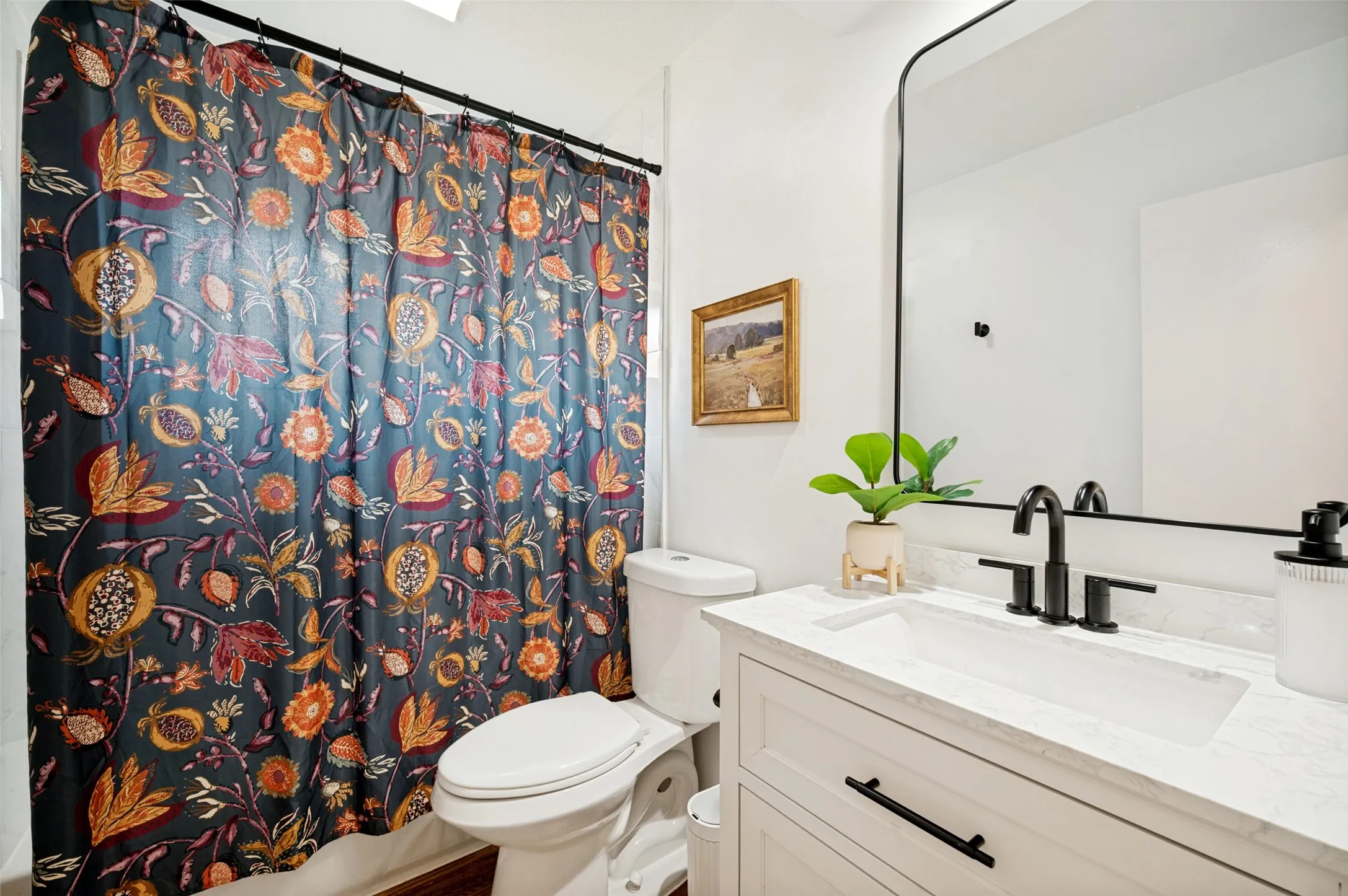 Full Bath with Tub/Shower combination, White Vanity and decorative countertop and integrated sink, matte black faucet, and a large black-framed mirror