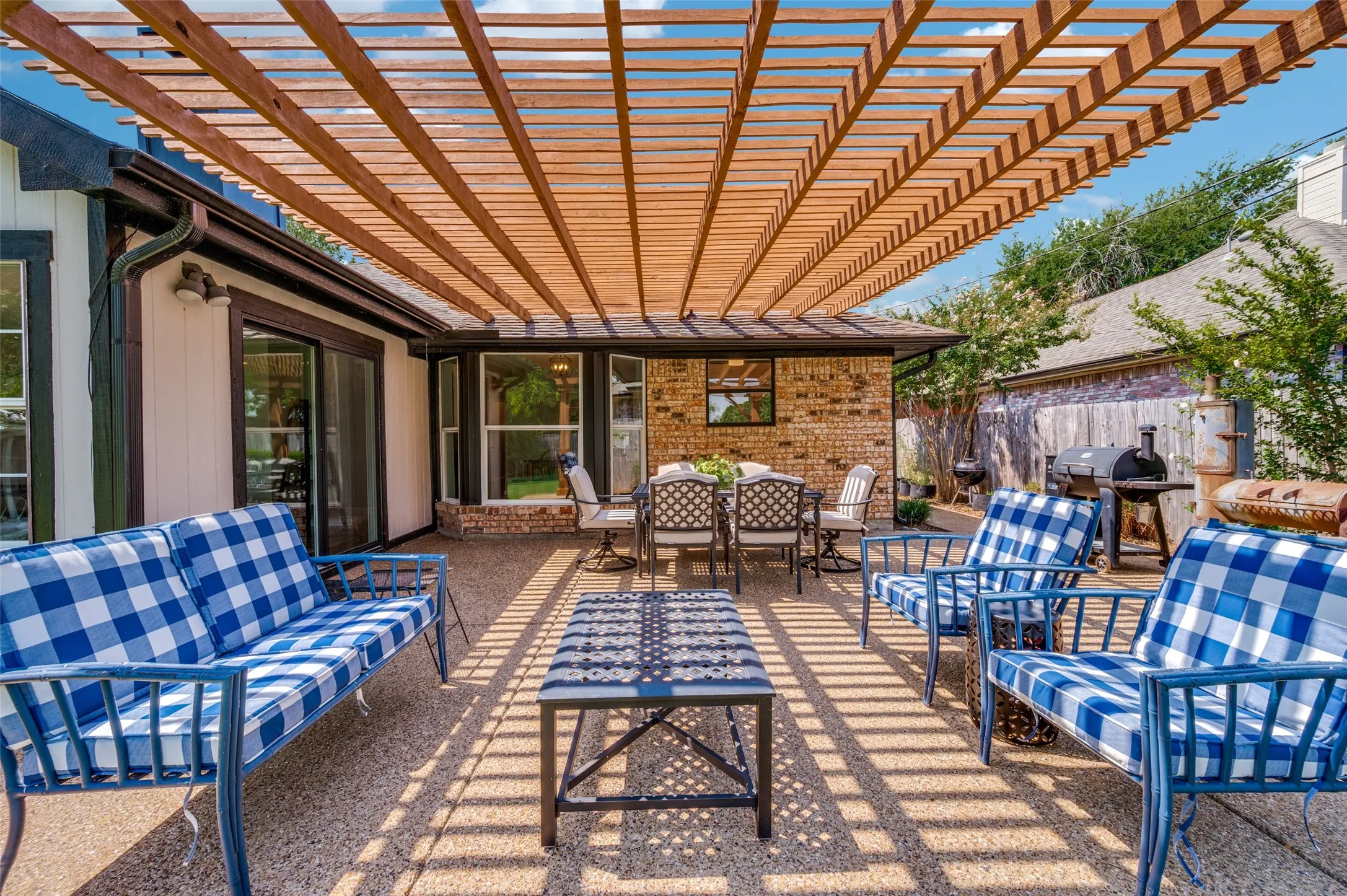 Expansive patio featuring an open-slat pergola, exposed aggregate concrete flooring, and direct access to interior spaces through sliding glass doors