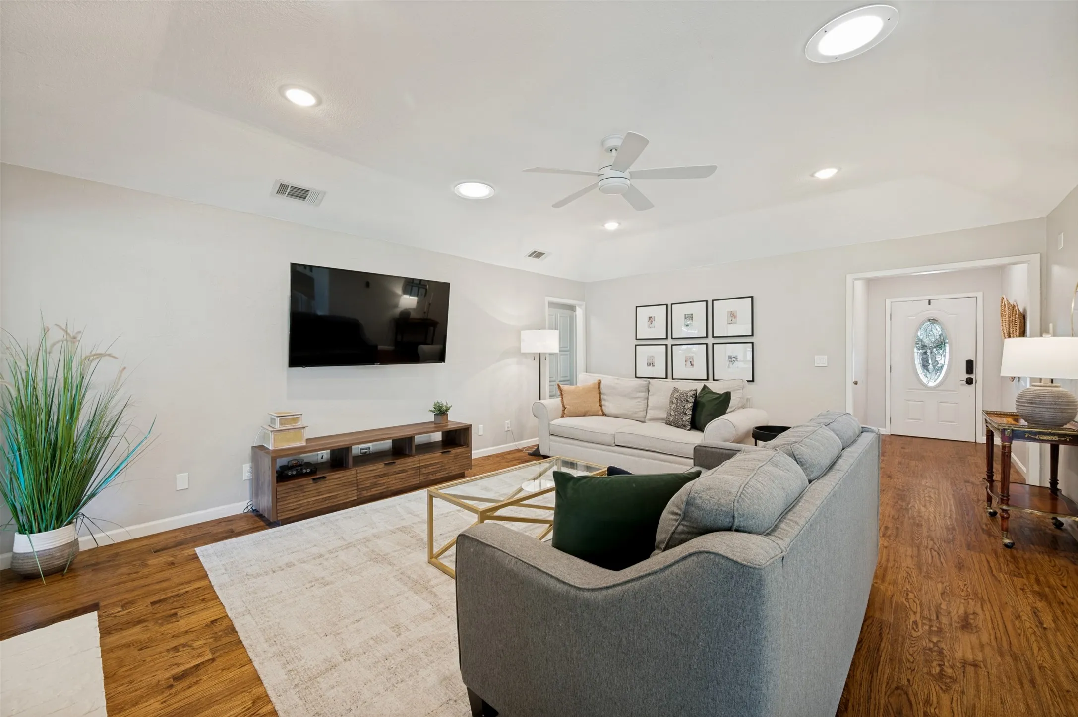 Living space featuring tall ceilings, lightly scrapped wood flooring, ceiling fan, and a white paneled entry door with oval glass insert