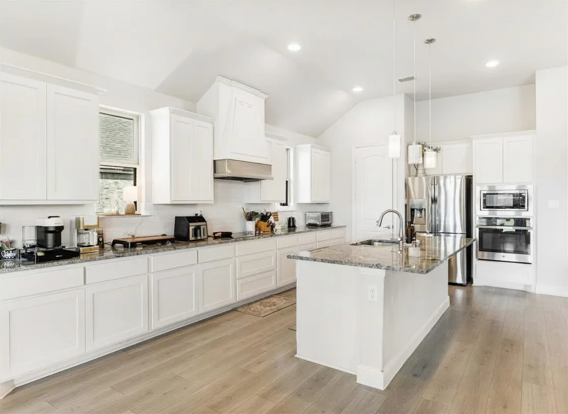 Kitchen featuring white shaker-style cabinetry, granite countertops, wood-finish flooring, a stainless steel appliance suite, and a central island with pendant lighting