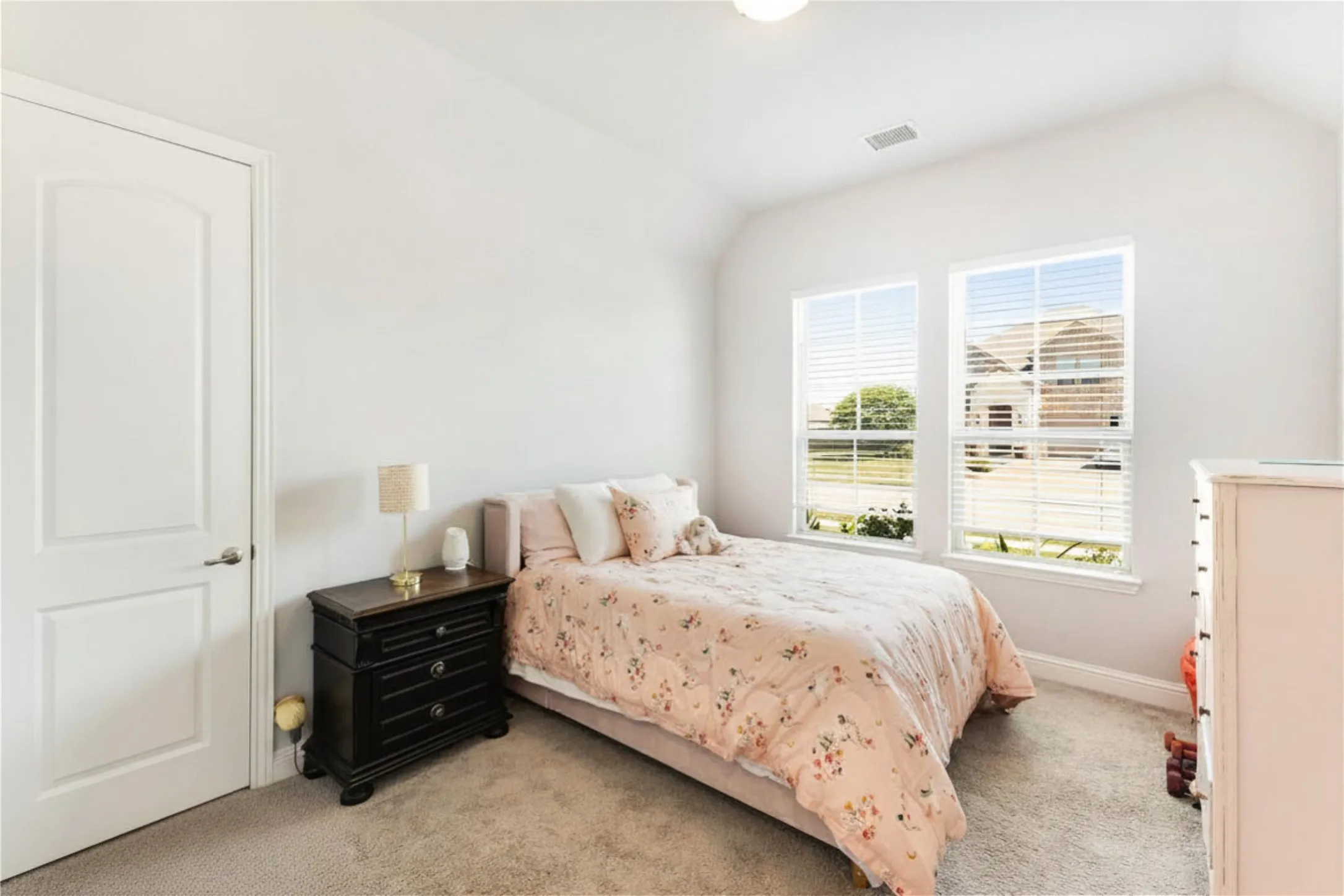 Carpeted room with a vaulted ceiling and two large windows with blinds