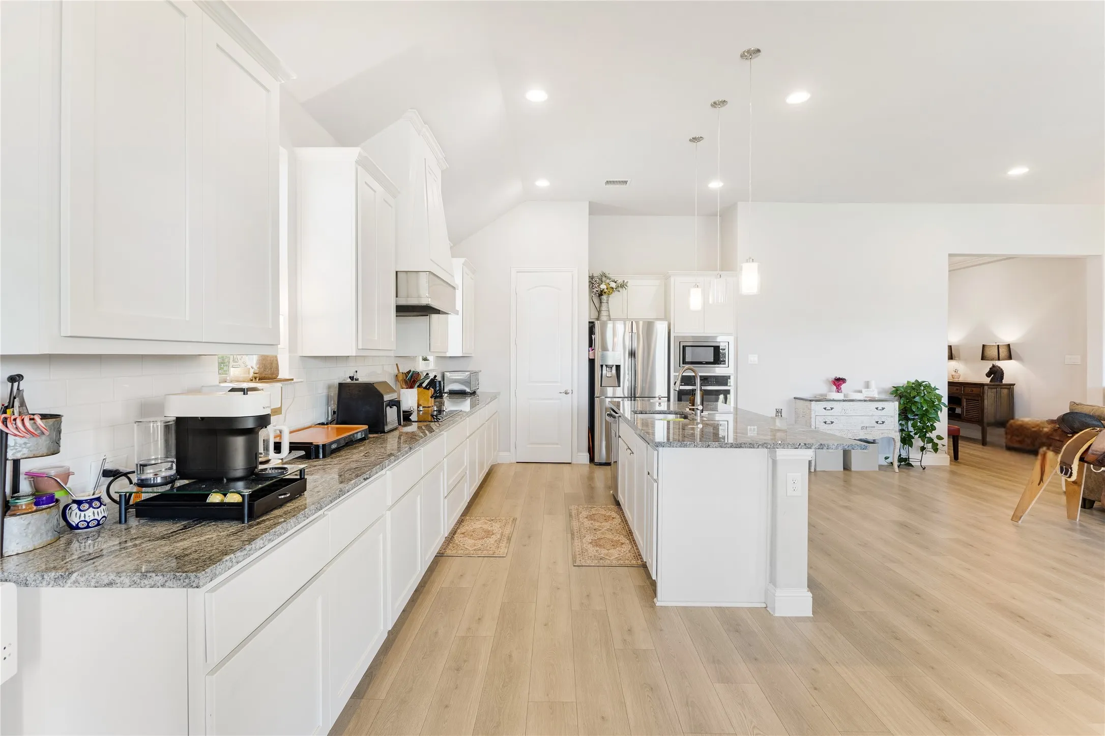 Modern kitchen featuring white cabinetry, light wood-finish flooring, recessed lighting, a central island with pendant lights, and stainless steel appliances