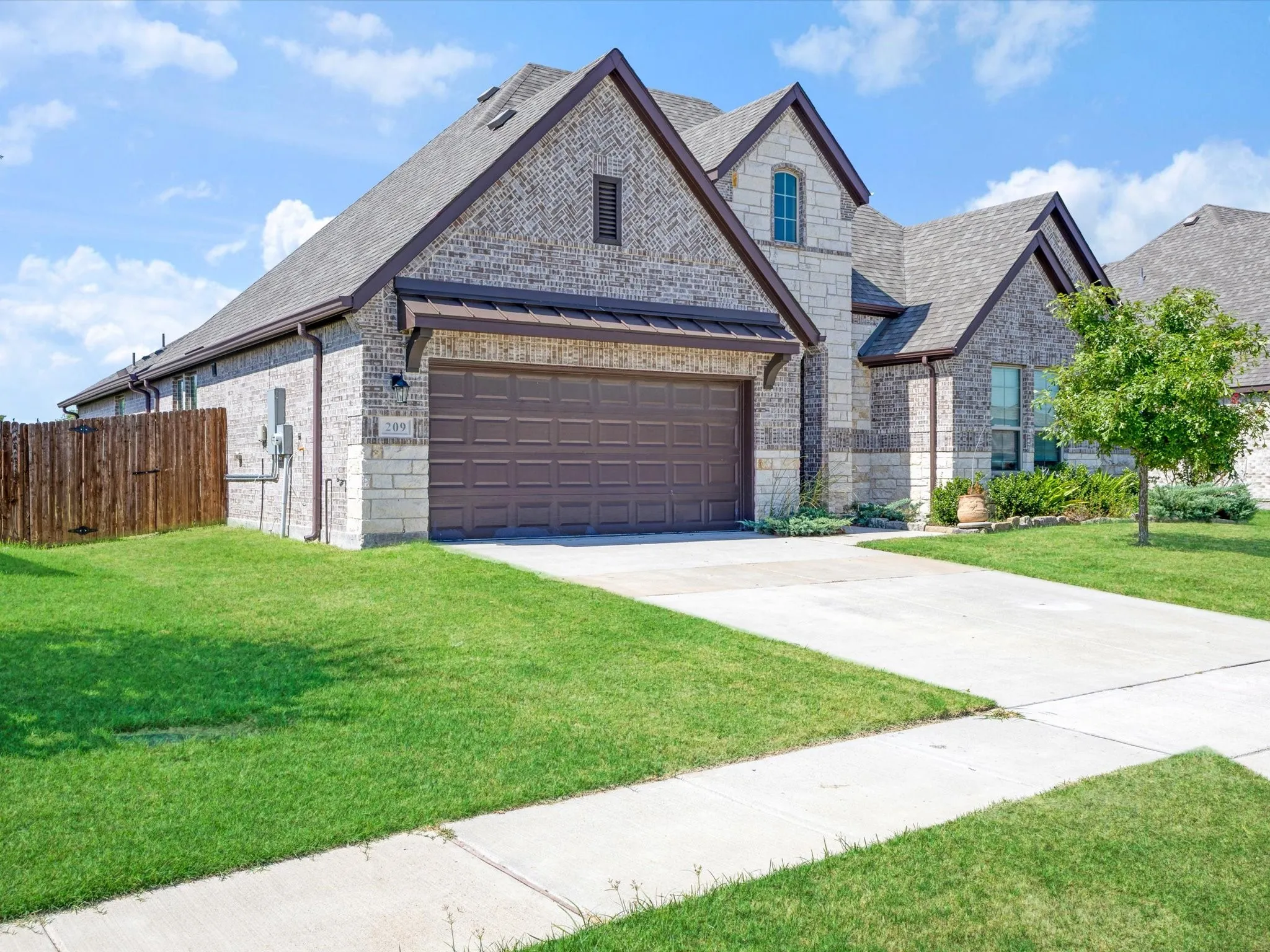 Brick and stone facade featuring a two-car garage with a paneled door, pitched rooflines, and a concrete driveway