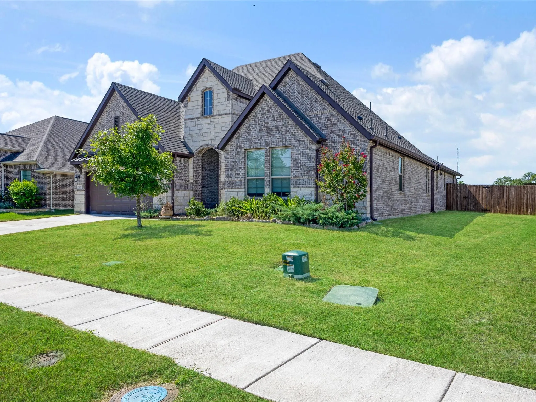 Exterior featuring a blend of brick and stone masonry, a dark shingle roof, arched entry, and a two-car garage
