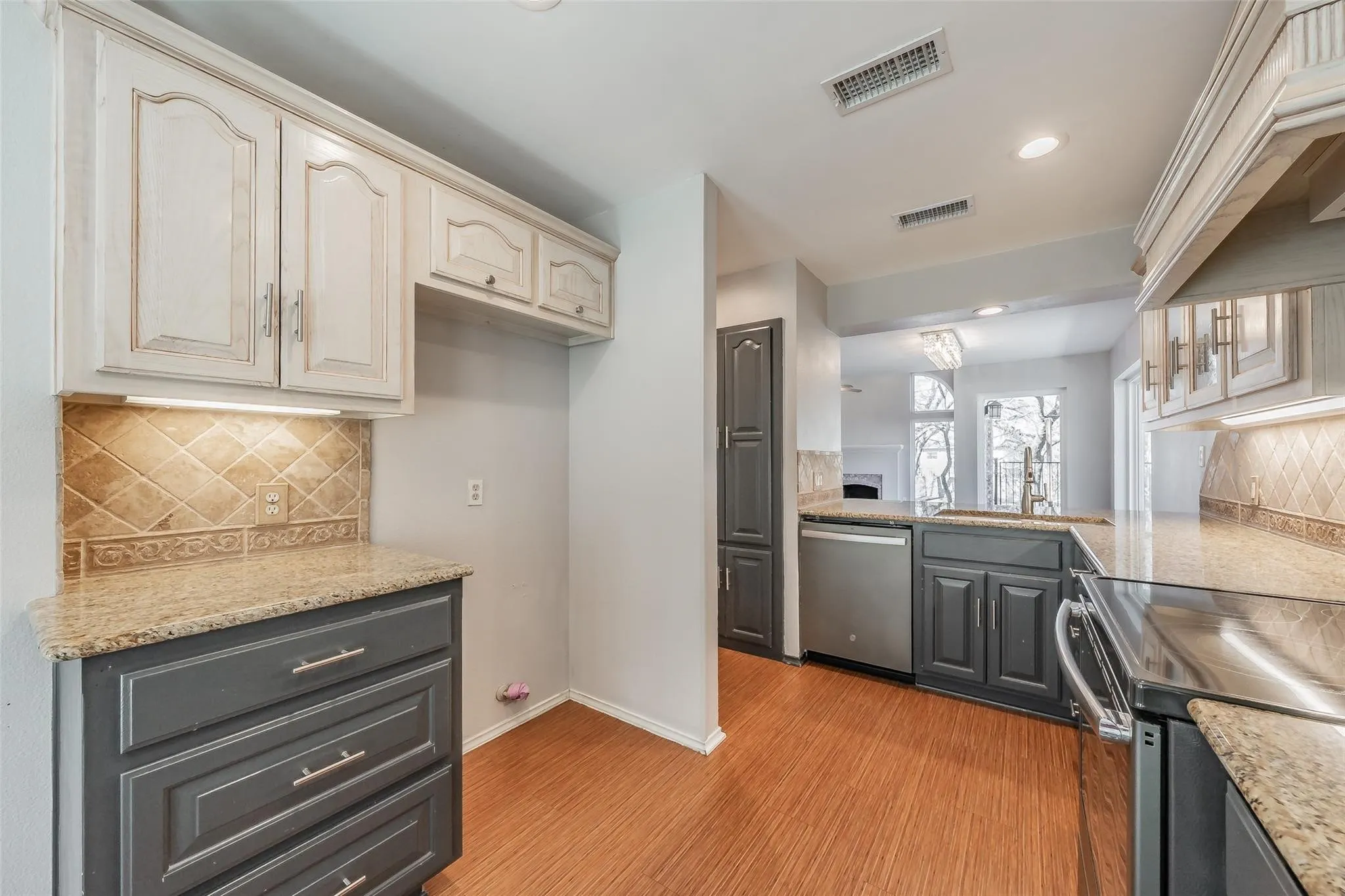 Kitchen featuring two-tone cabinetry, granite countertops, tile backsplash, stainless steel appliances, and wood-finish flooring