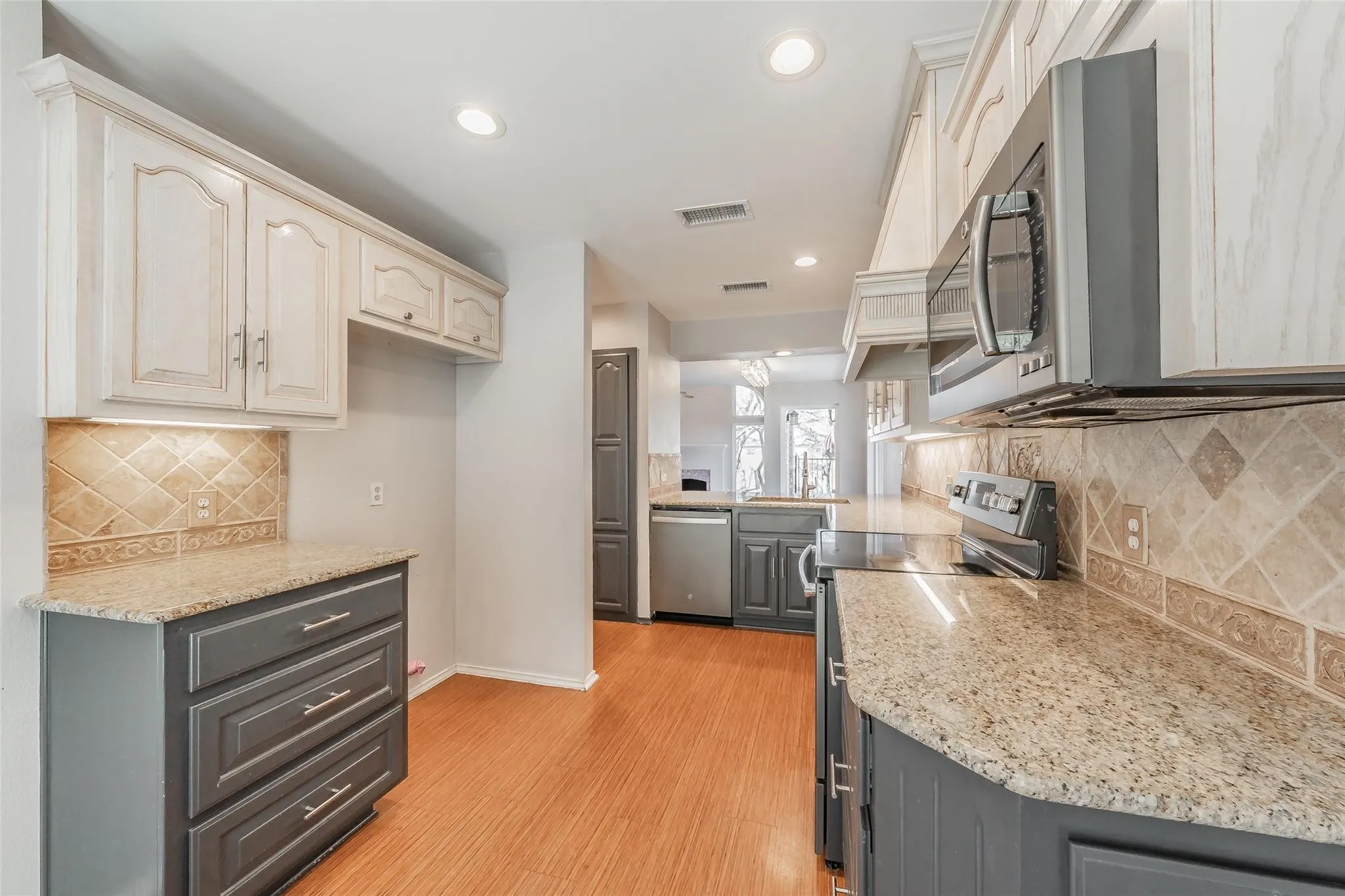 Kitchen featuring light-toned upper cabinetry, dark lower cabinetry, stainless steel appliances, granite countertops, and a tiled backsplash