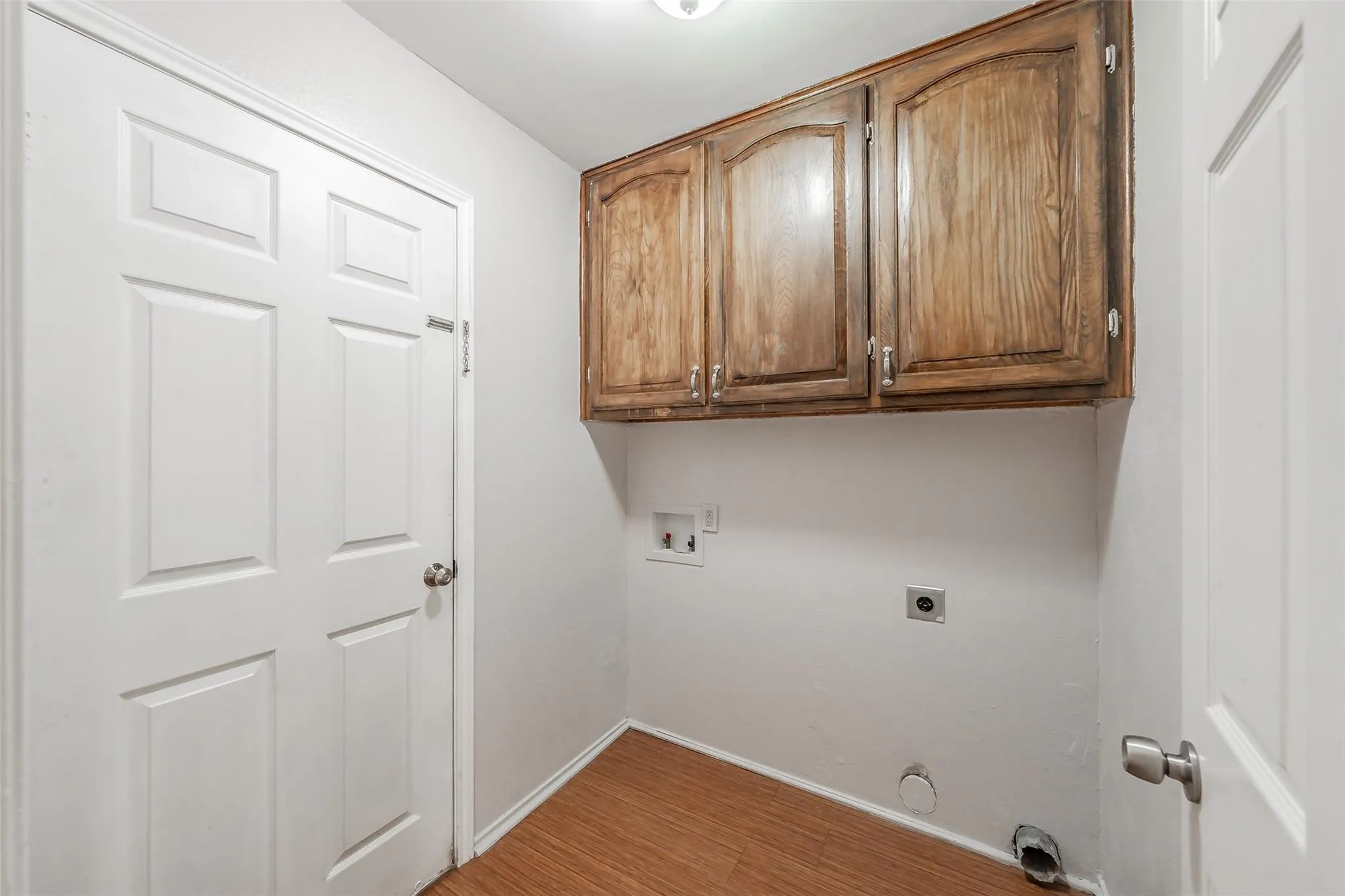Wood-finish flooring with baseboards, overhead cabinetry, and appliance connections