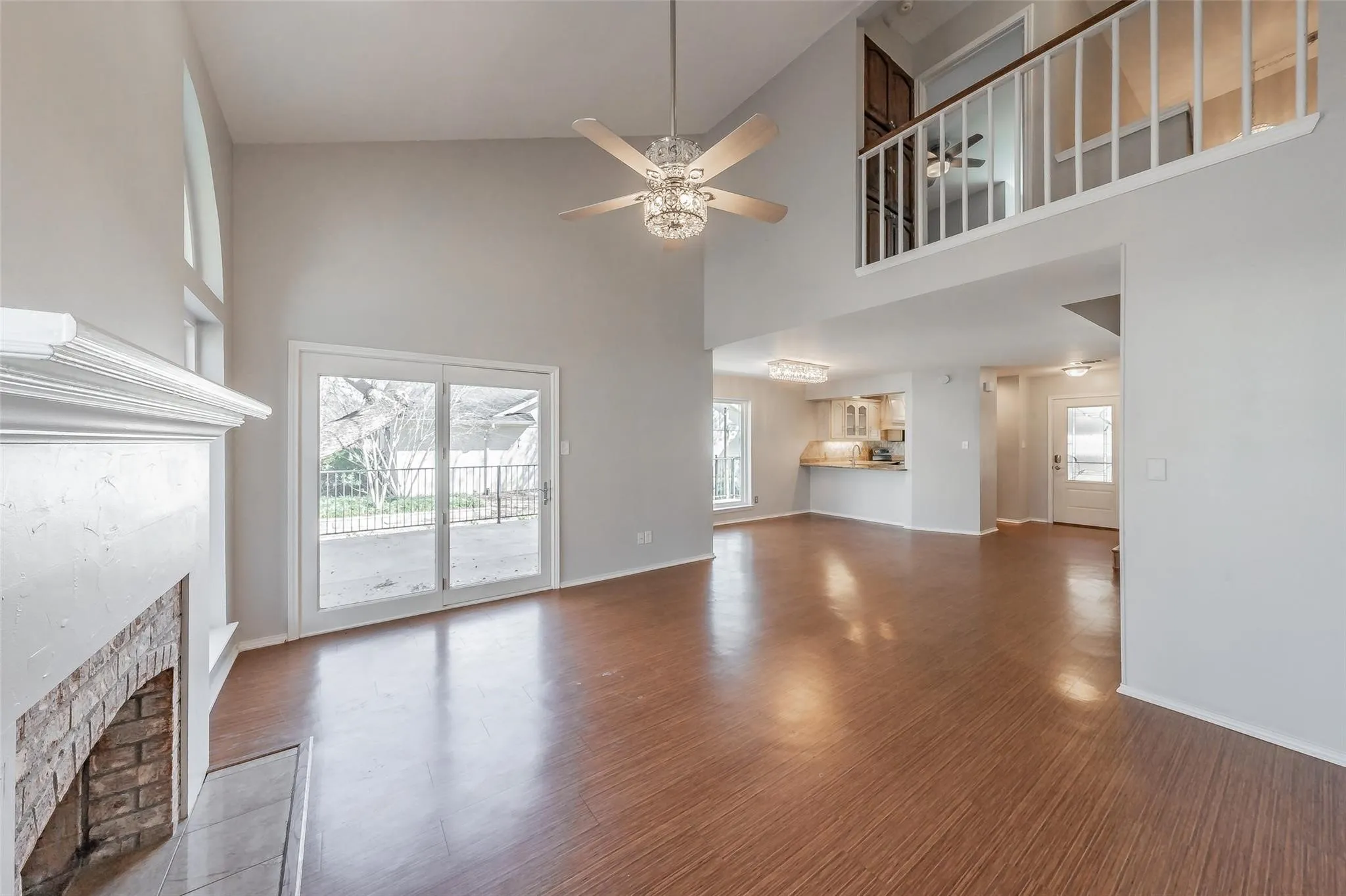 Spacious living area featuring high ceilings, wood-finish flooring, a brick fireplace with a white mantel, and sliding glass doors opening to the exterior