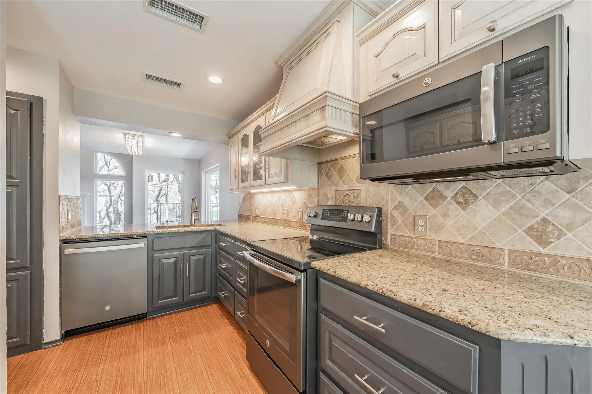 Kitchen featuring granite countertops, stainless steel appliances, wood-finish flooring, two-tone cabinetry, and an ornamental tile backsplash
