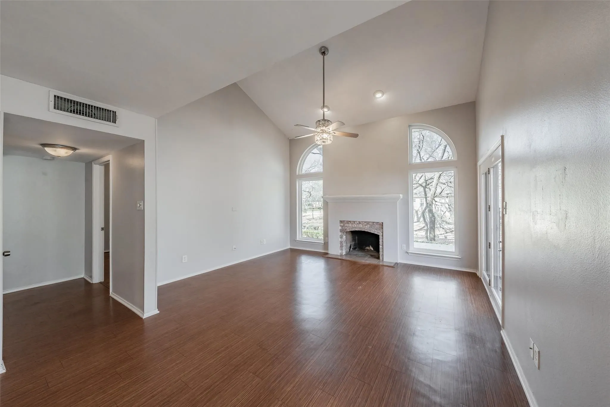 Living area featuring wood-finish flooring, vaulted ceilings, and a fireplace with a brick surround