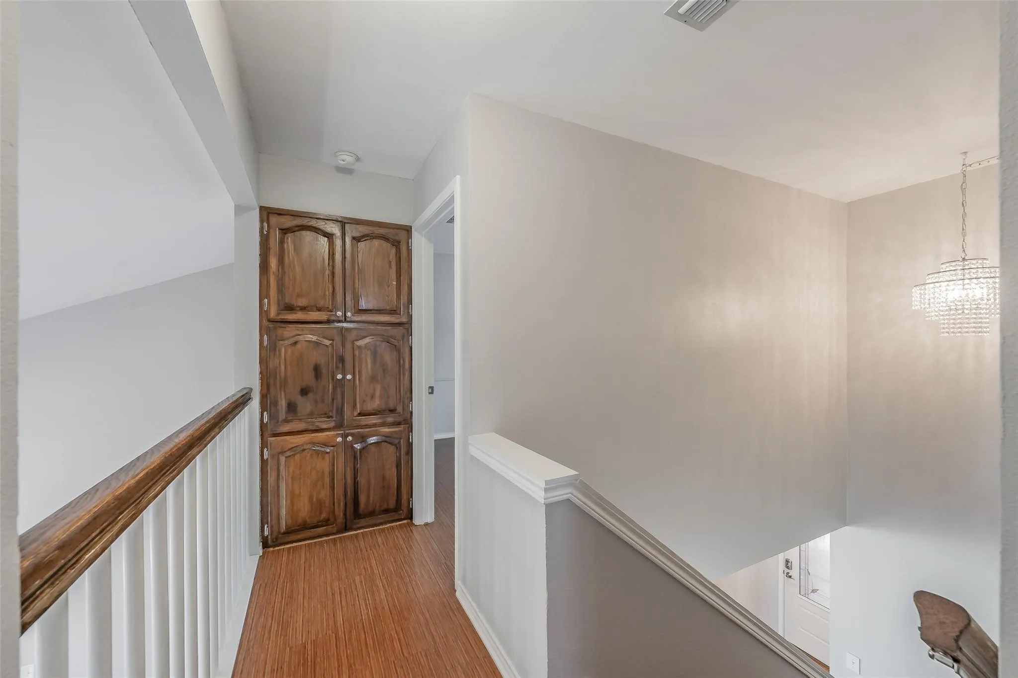 Hallway featuring built-in wood cabinetry, wood-finish flooring, and white railing with wood handrail