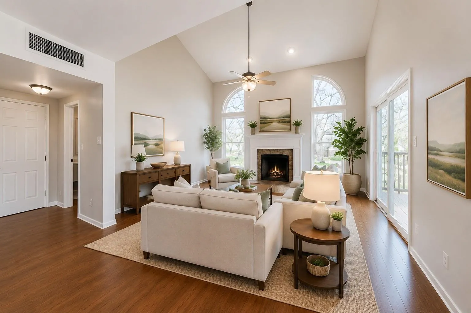 Vaulted living space featuring wood-finish flooring, a fireplace with a white mantel, and arched windows