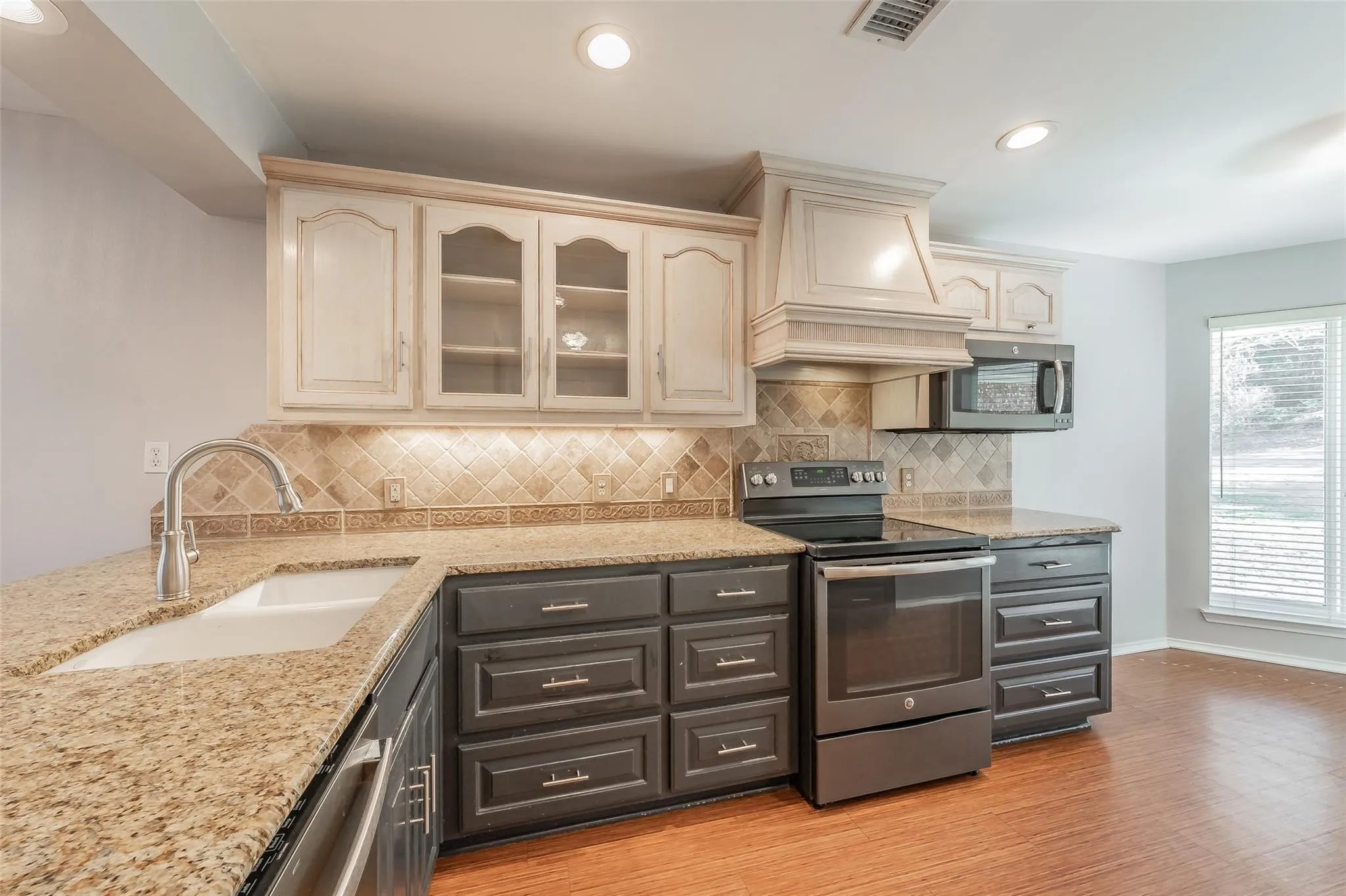 Kitchen featuring wood-finish flooring, two-tone cabinetry with upper glass-front doors, granite countertops, and a full tile backsplash