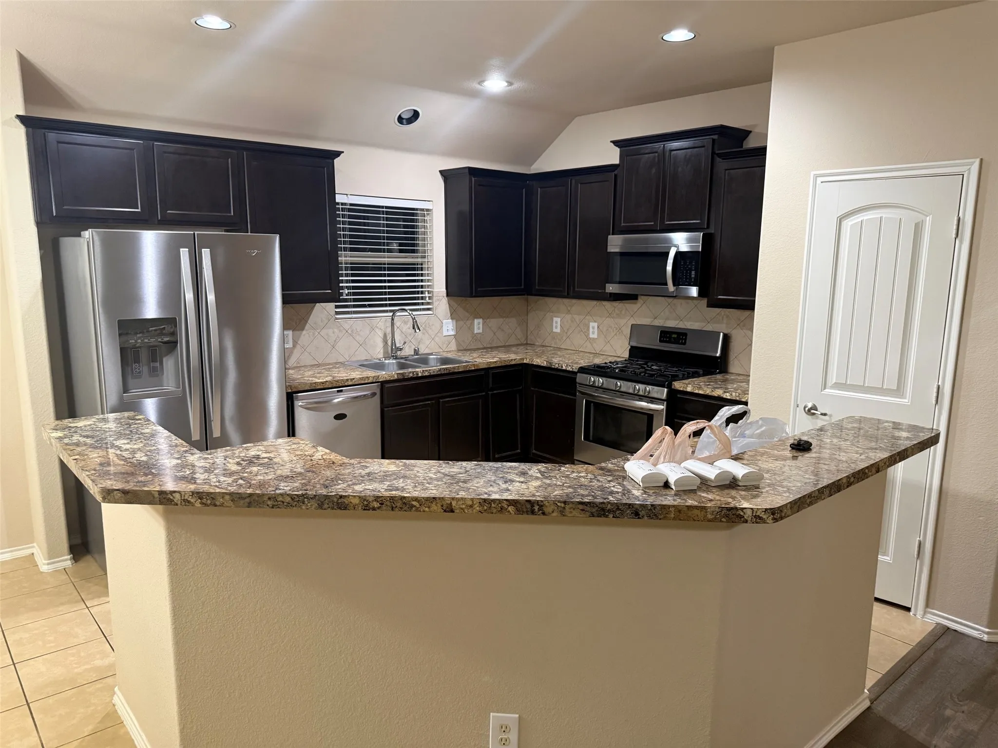 Kitchen featuring dark wood cabinetry, stainless steel appliances, a tile backsplash, and granite countertops with a breakfast bar