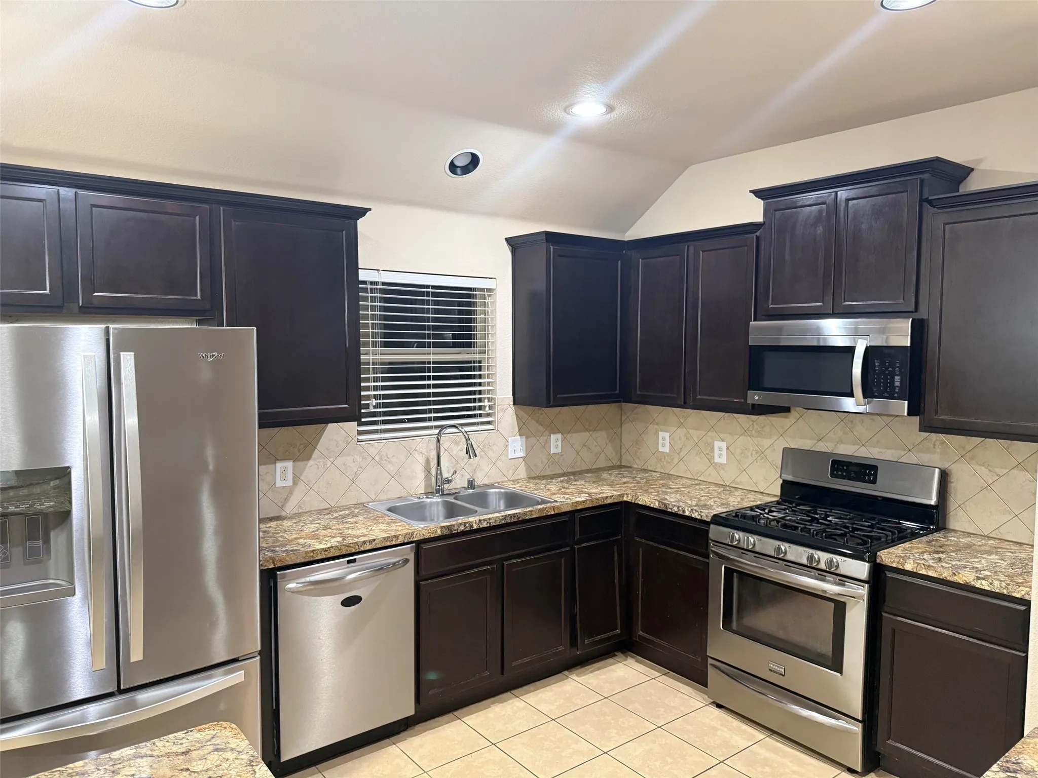 Kitchen featuring dark wood cabinetry, stainless steel appliances, speckled countertops, a tile backsplash, and recessed lighting