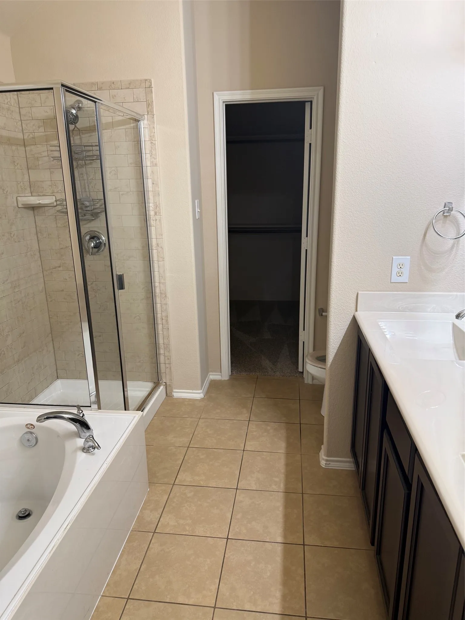 Bathroom featuring a built-in soaking tub with polished chrome fixtures, a glass-enclosed shower with tile surround, and a dual-sink vanity with dark wood cabinetry and light-toned countertops