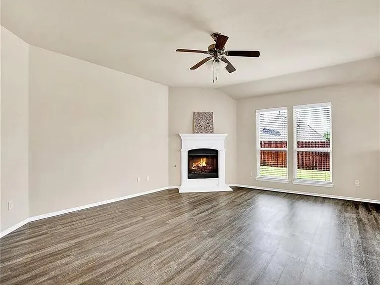 Living area featuring a corner fireplace with a white mantel, wood-finish flooring, and multiple windows with blinds