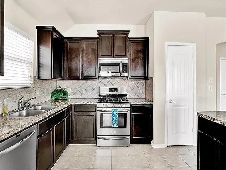 Well-appointed kitchen featuring dark wood cabinetry, granite-style countertops, stainless steel appliances, a tiled backsplash, and light-toned tile flooring