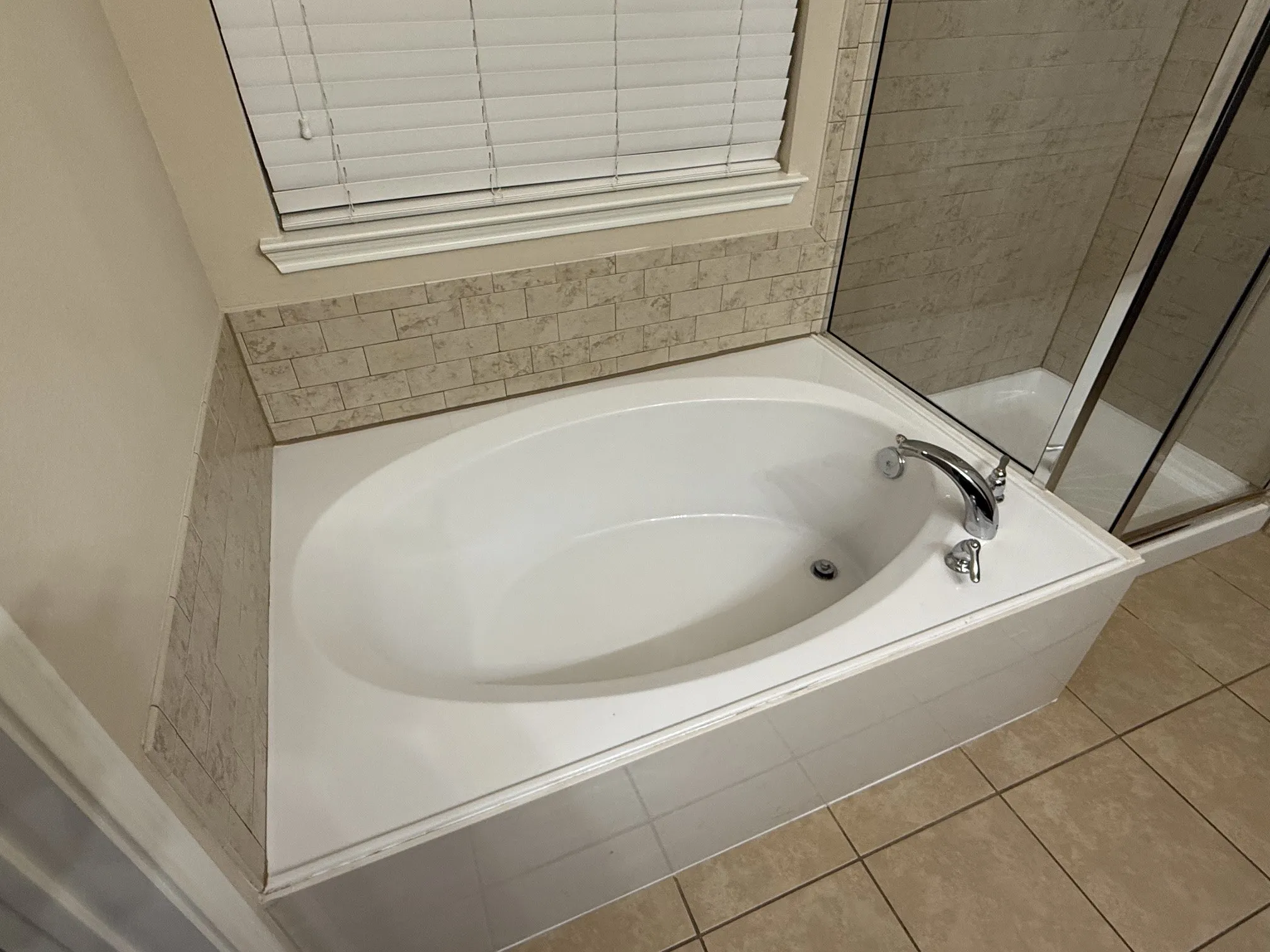 Built-in soaking tub with deck-mounted chrome fixtures, surrounded by neutral-toned subway tile