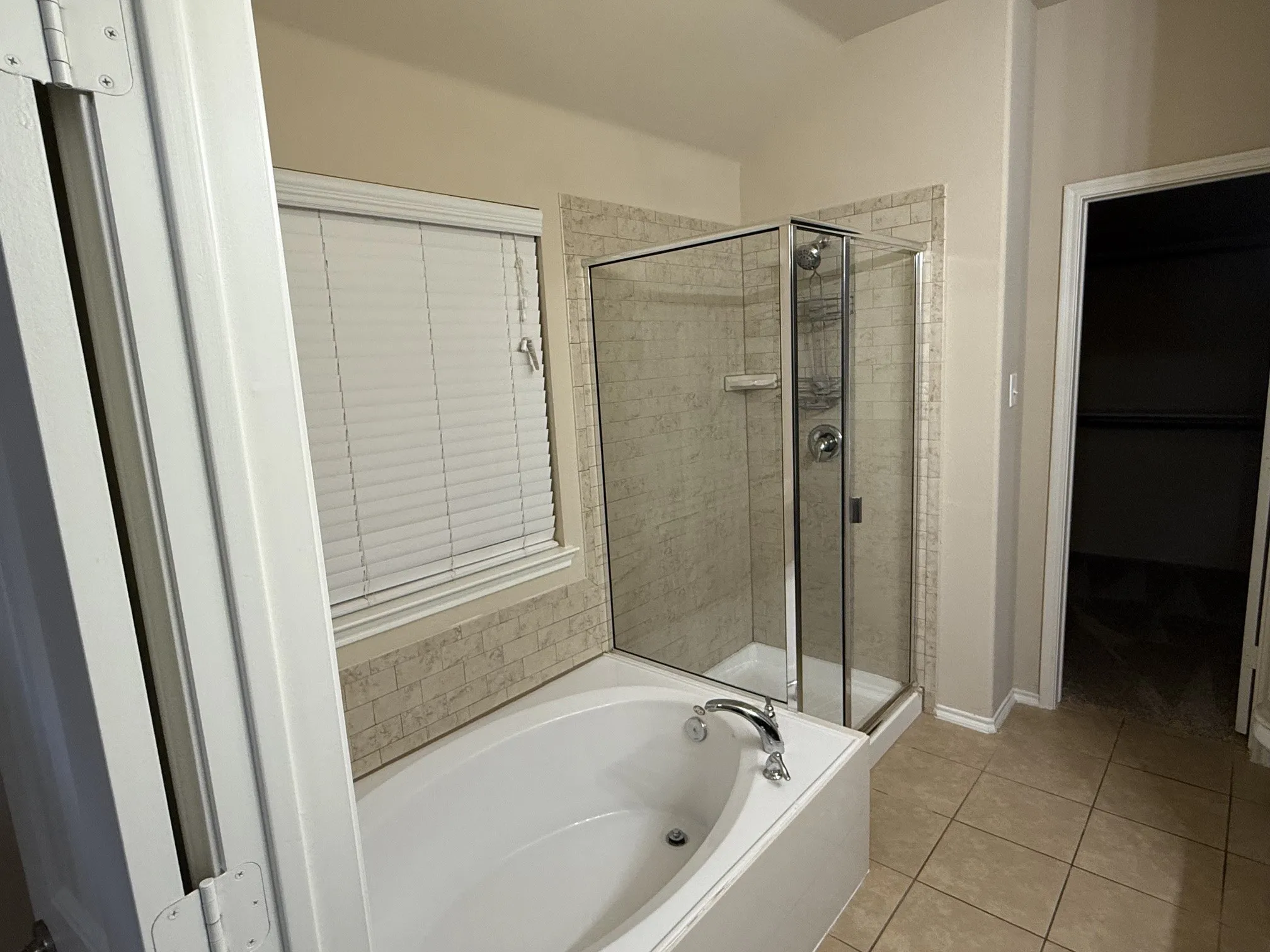 Bathroom featuring a built-in tub with chrome fixtures, a glass-enclosed shower with tile surround, and neutral tile flooring