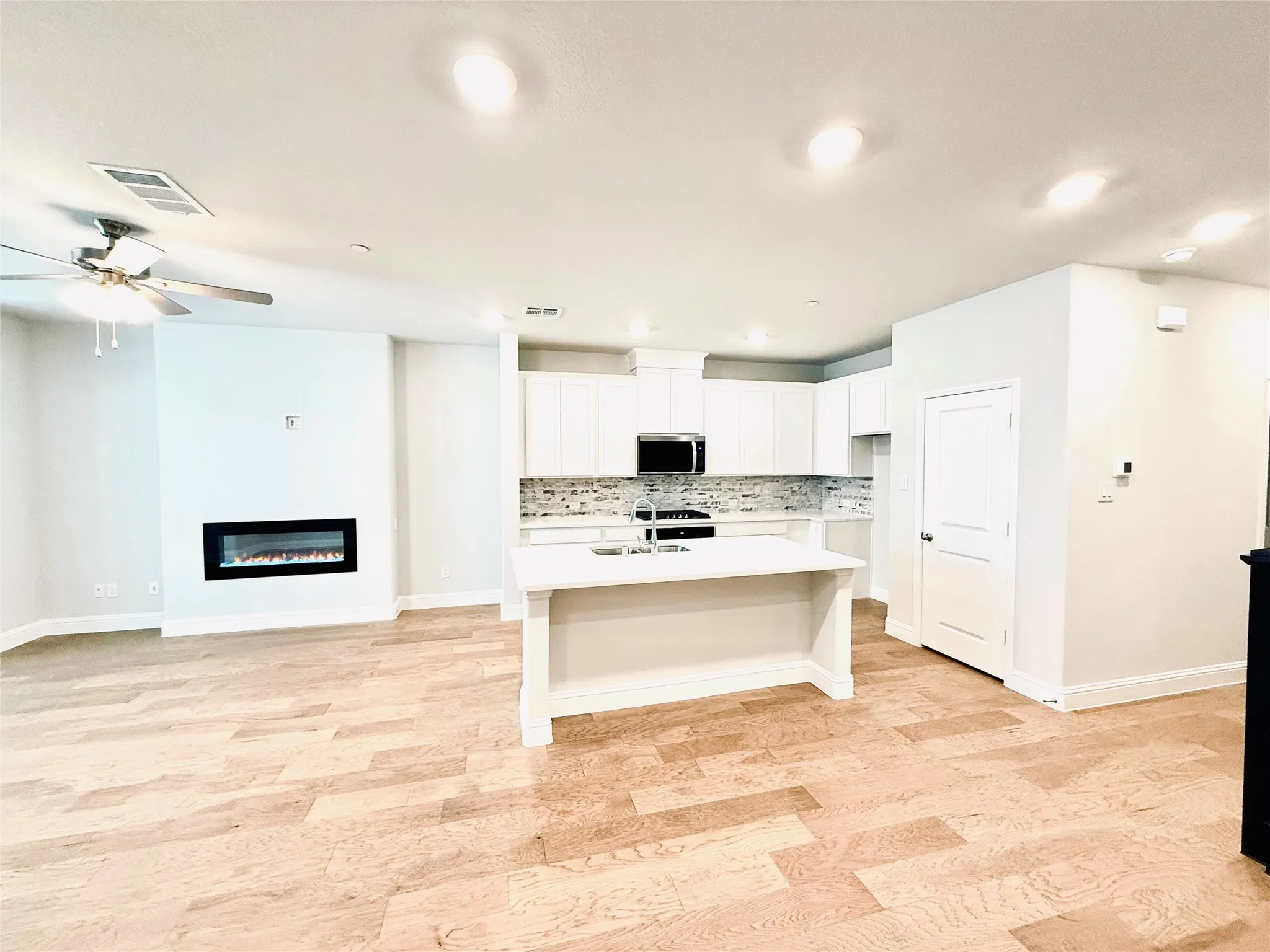 Open-concept living space featuring wood-finish flooring, an electric fireplace, recessed lighting, a ceiling fan, and a kitchen island with built-in sink