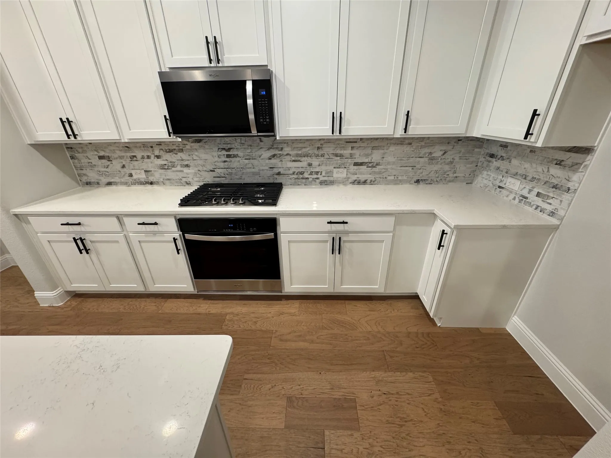 Kitchen featuring white cabinetry with matte black hardware, stone tile backsplash, white countertops, a built-in gas range, and wood-finish flooring