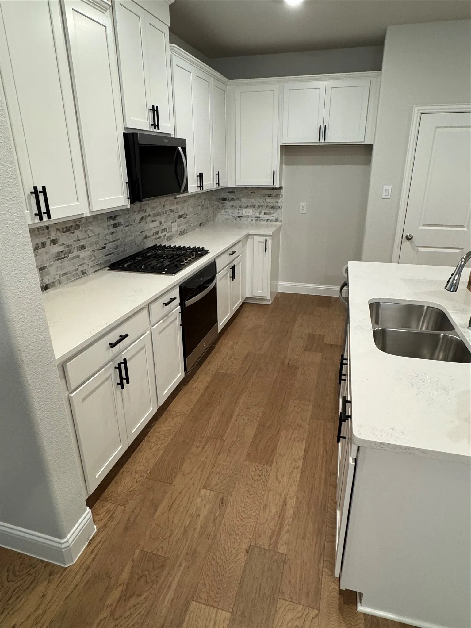 Modern kitchen featuring wood-finish flooring, white cabinetry, matte black hardware, stone-look countertops, and a subway tile backsplash