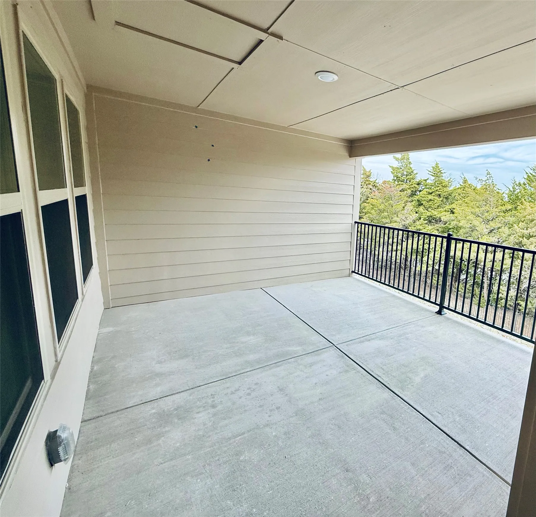 Covered patio featuring a concrete slab, horizontal siding, recessed lighting, and a black metal railing overlooking a tree line