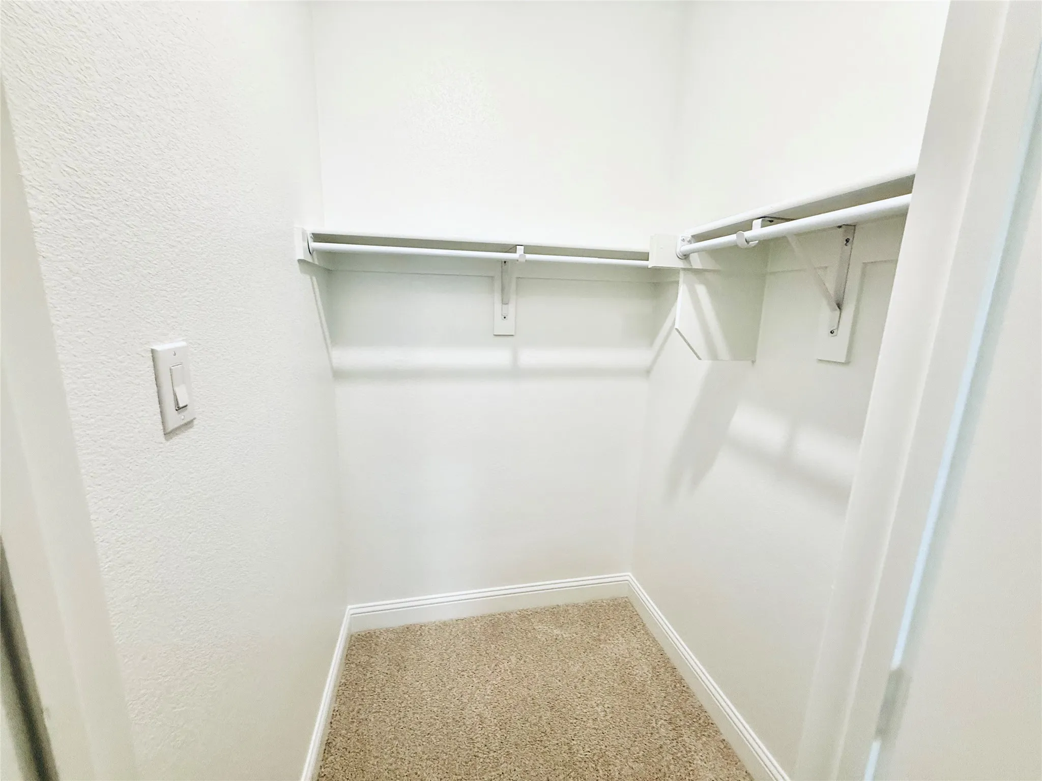 Walk-in closet featuring light-toned carpeting, white baseboards, and built-in shelving with hanging rods