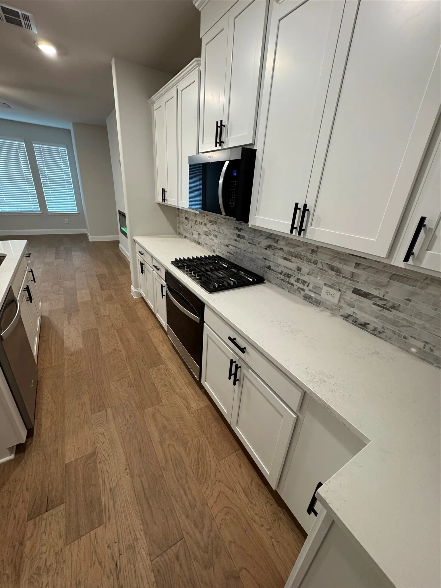 Modern kitchen featuring white shaker cabinetry with matte black hardware, white countertops, and a full-height tiled backsplash