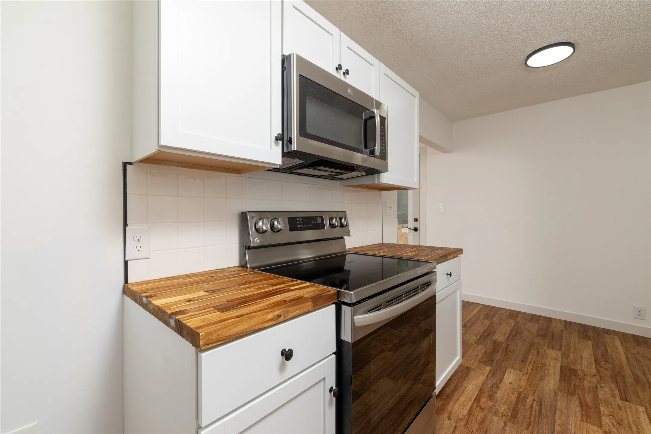 Kitchen featuring white shaker-style cabinetry, wood-finish countertops, subway tile backsplash, stainless steel microwave, and a stainless steel electric range