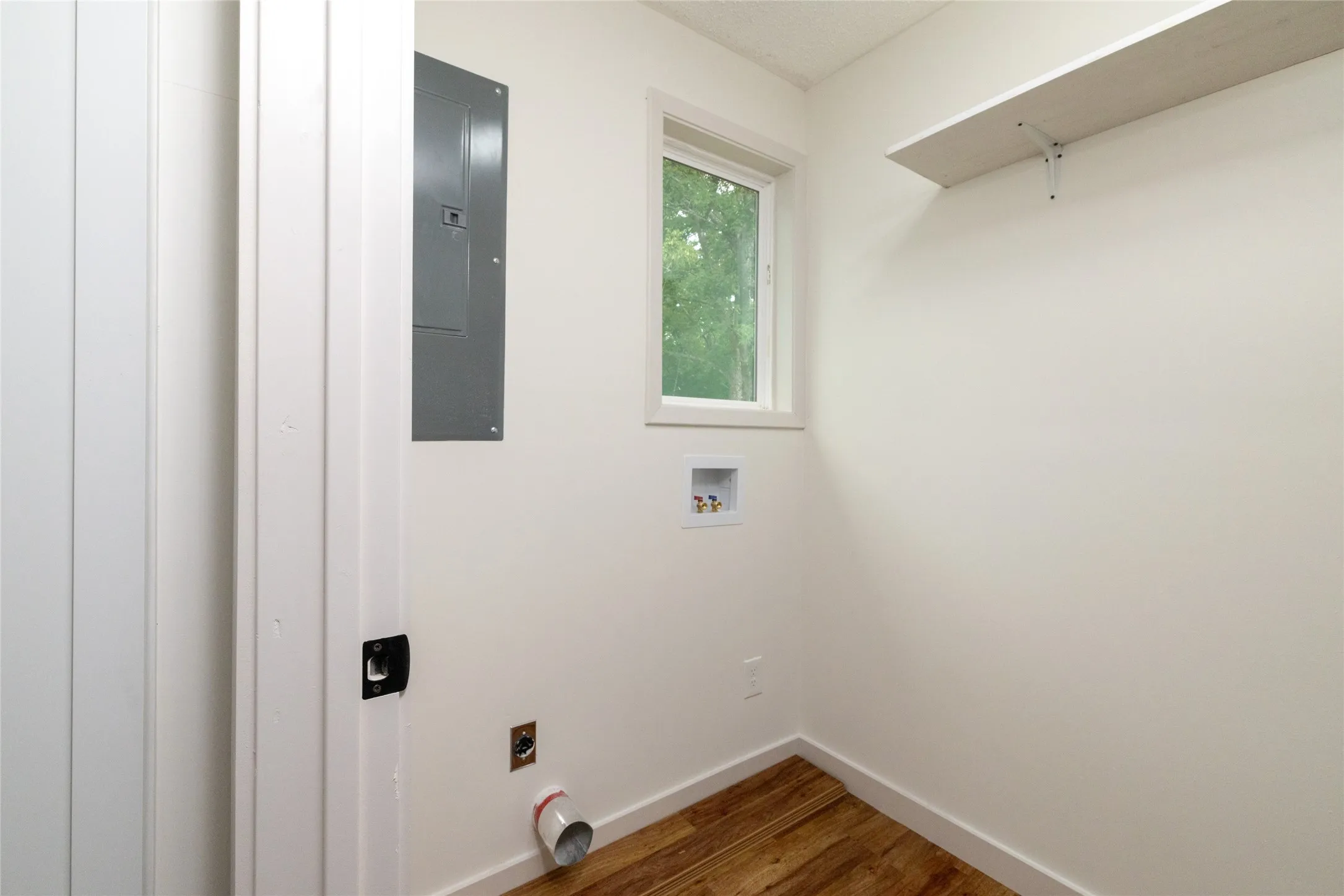 Dedicated utility space featuring wood-finish flooring, a single window, and a built-in shelving unit