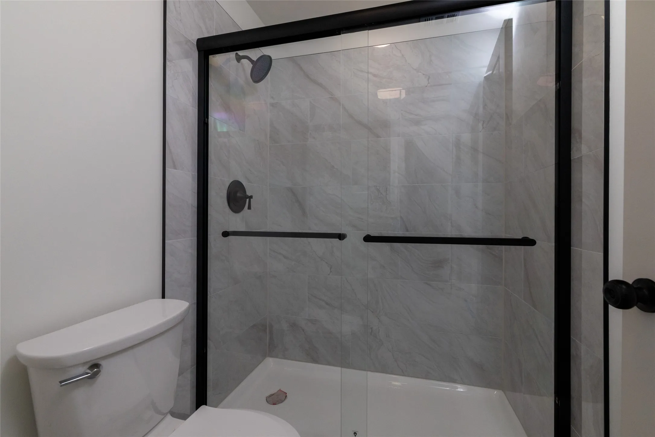 Shower enclosure featuring a matte black framed glass door, light-toned tiled walls, a white shower pan, and a matching matte black shower head and controls