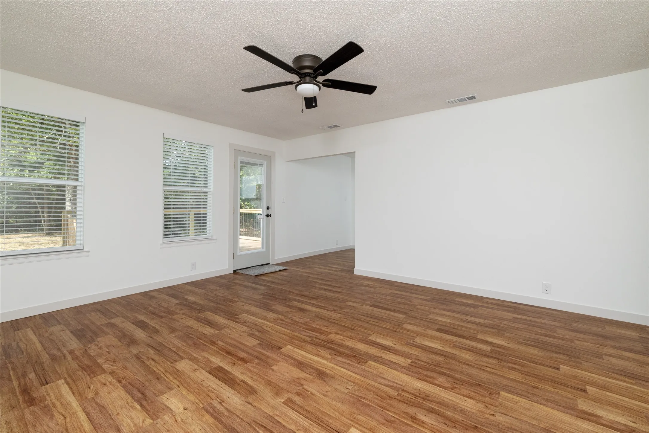 Spacious interior room featuring wood-finish flooring, white walls, and a ceiling fan with integrated lighting