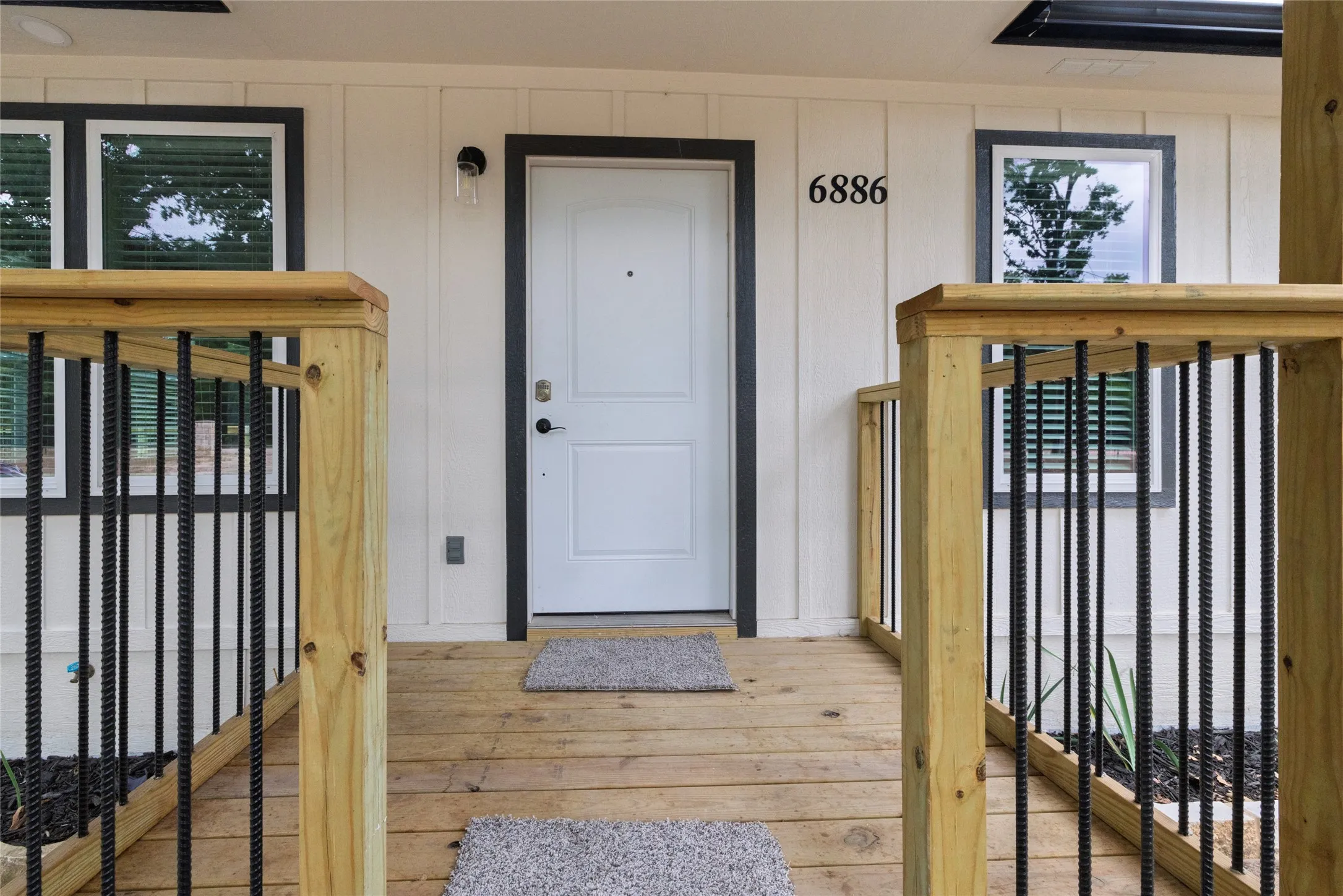 Front entry featuring a white paneled door with dark trim, wood-finish decking, and wood railings with black metal balusters